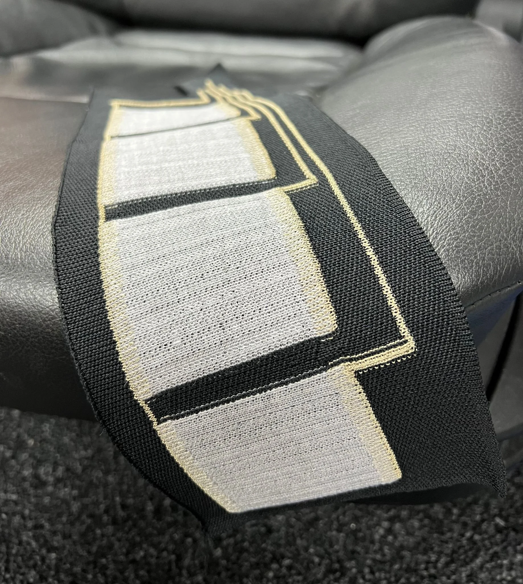 Close-up of a knitted sensor using conductive yarn in black, white, and beige, sewn onto a grey textured surface.