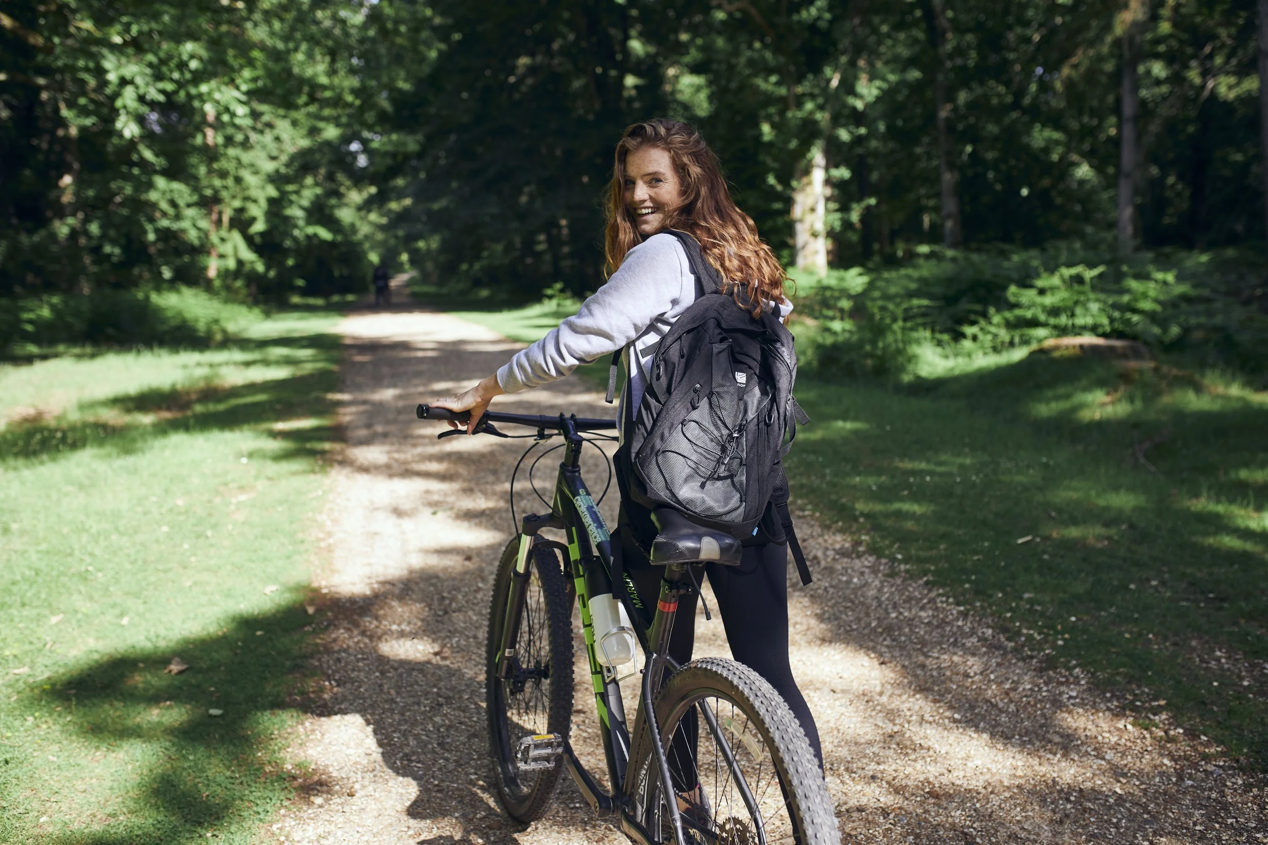 A women pushed a mountain bike down a rocky path in a wood. Lifestyle photography by Jon Enoch.