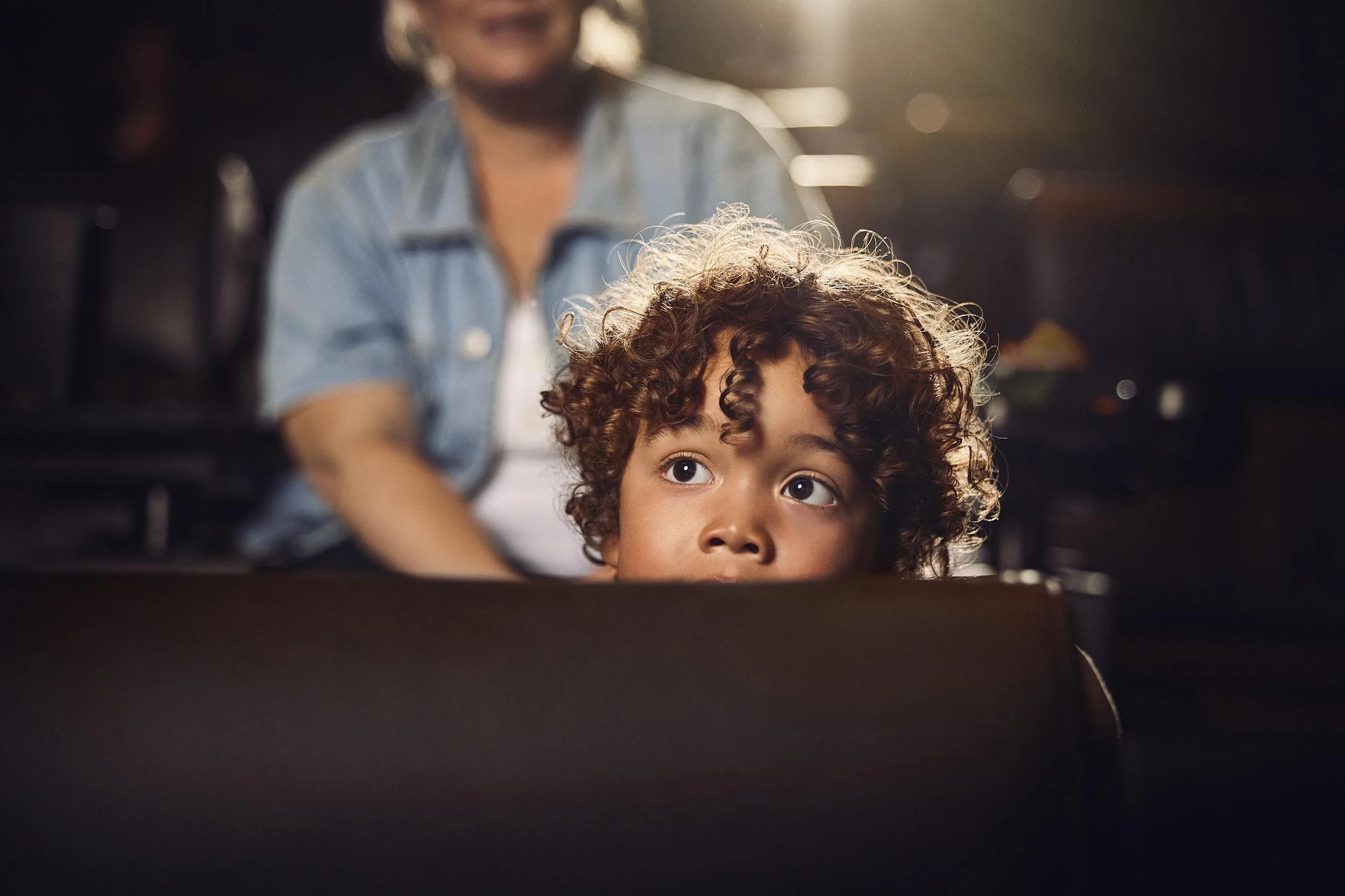 A young boy peeks over the cinema chair at the movie in this lifestyle image by photographer Jon Enoch
