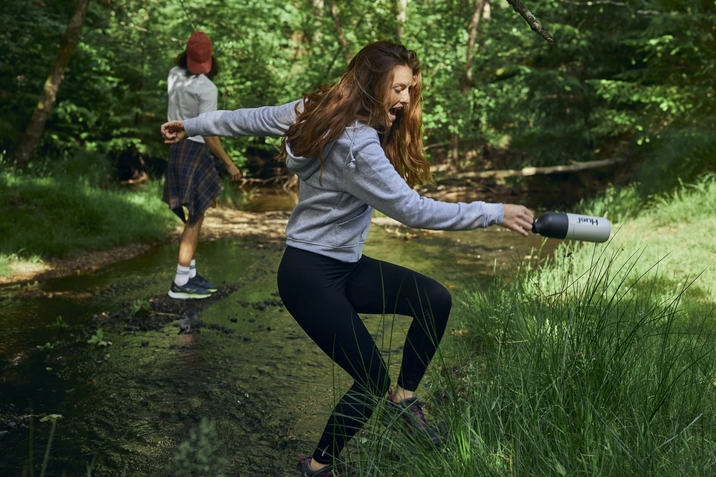 Friends smile as cross a small steam in a woods. Lifestyle photography by Jon Enoch