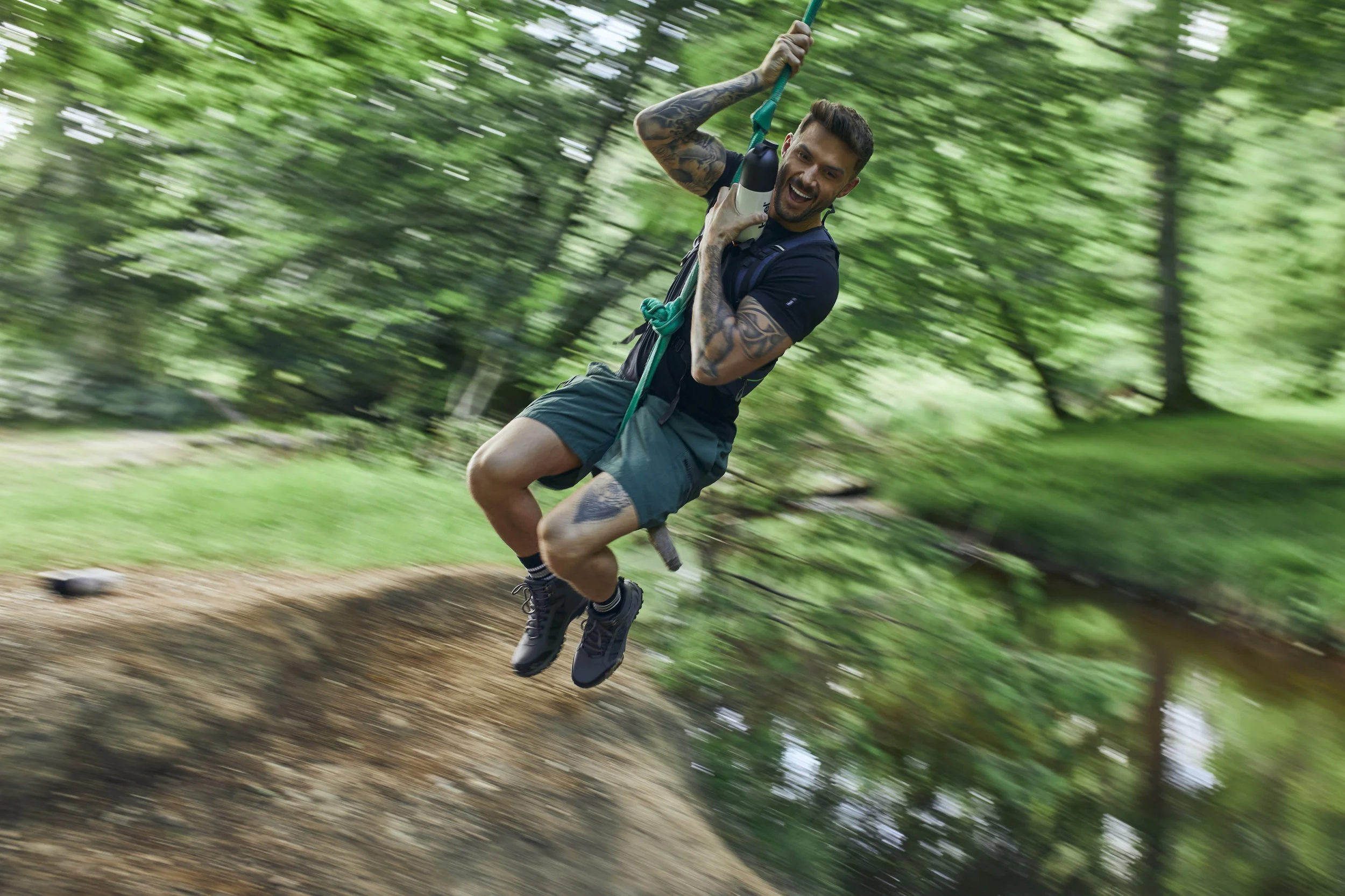 A man plays of a rope swing. Swinging over a river in the New Forest. Photography by lifestyle photographer Jon Enoch