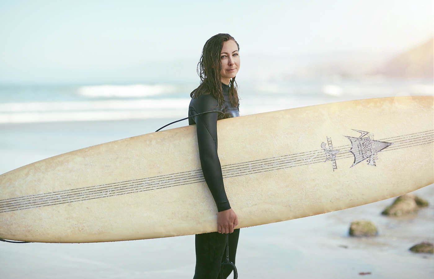Sport lifestyle photographer Jon Enoch photographs a young women with her long board on the beach in California as the morning sun rises over the beach.