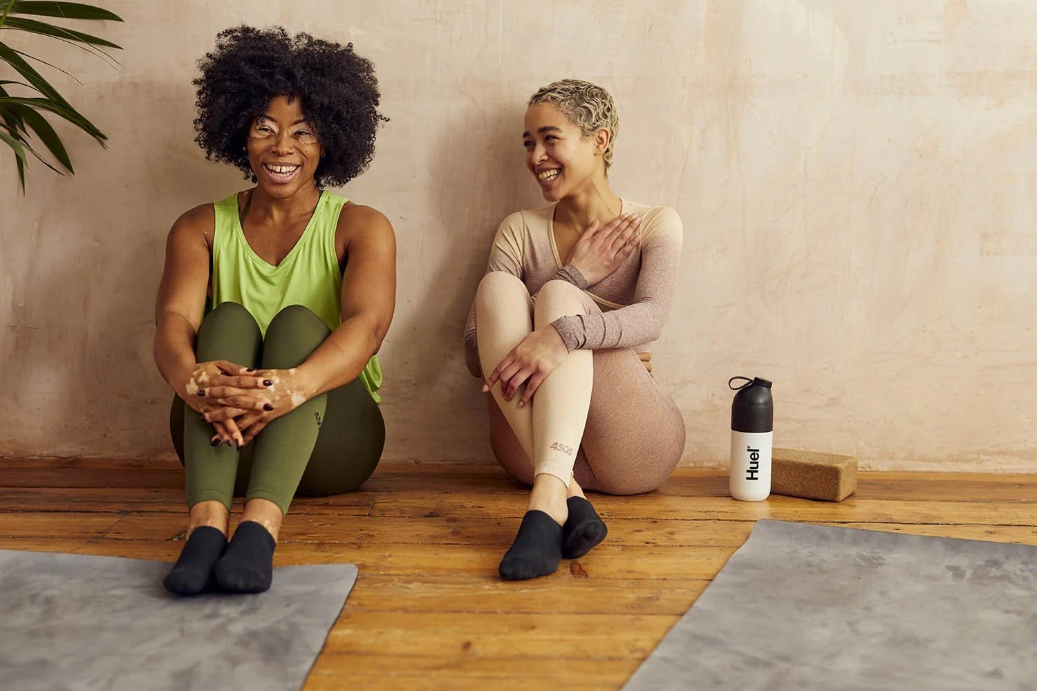 Two women chat at the end of a yoga class; a bottle of Huel sits next to them in this lifestyle image by London photographer Jon Enoch