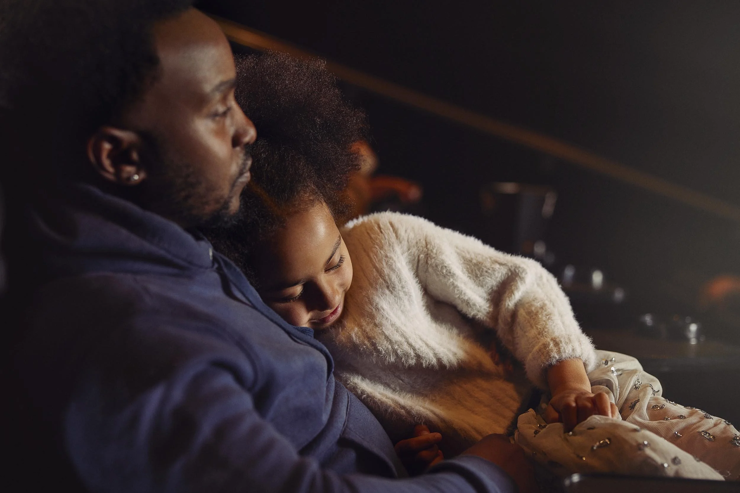 A young girl sleeps on her dads lap whilst he watches a film in this lifestyle photography by London based advertising photographer Jon Enoch for leading cinema chain Vue