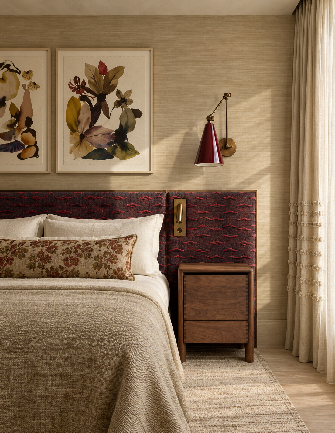 Warmly lit modern bedroom with floral artwork, burgundy upholstered headboard, red wall sconce, wooden nightstand, cream bedding, and sheer curtains.