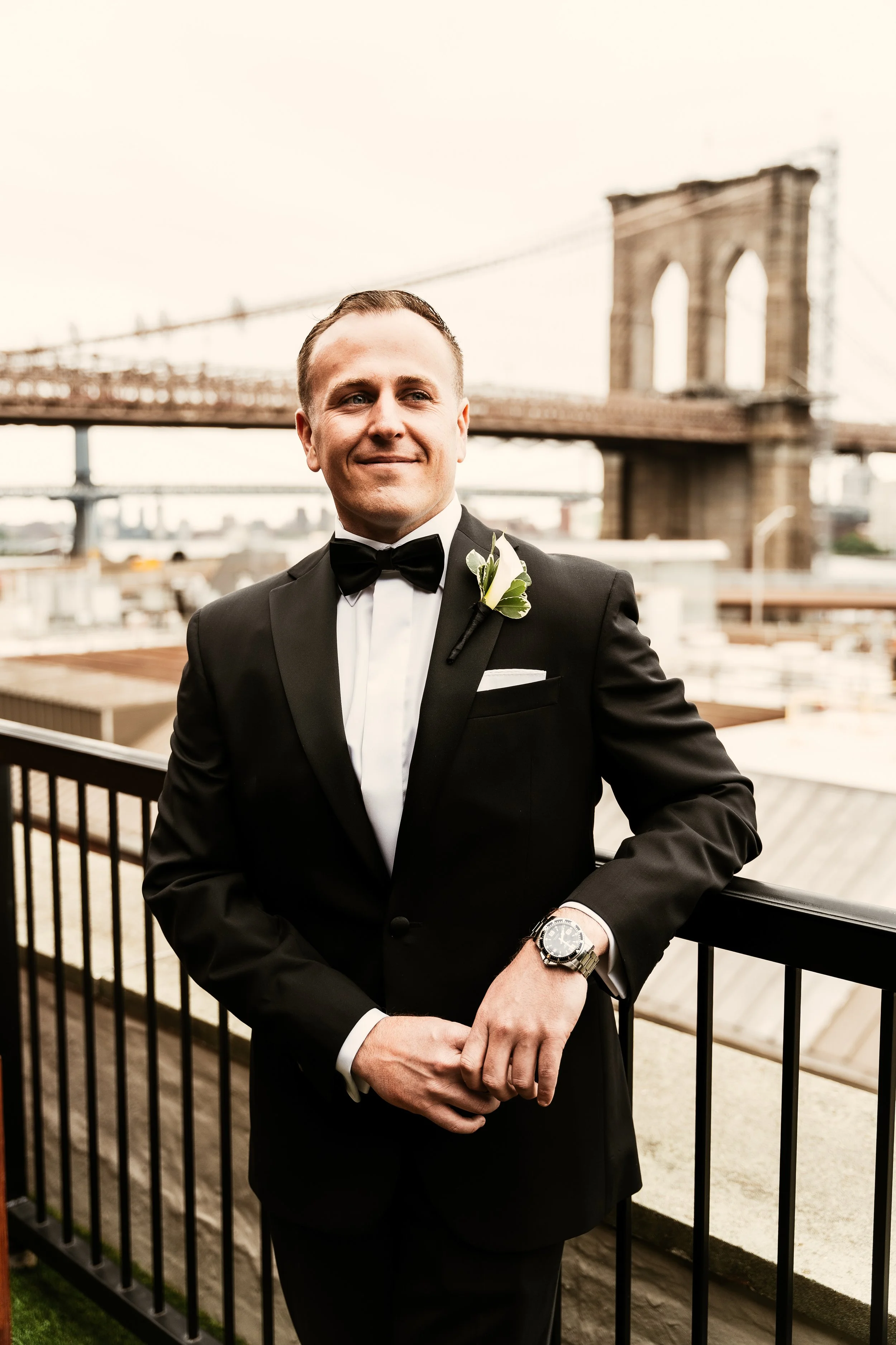 Groom smiling on a balcony overlooking the Brooklyn Bridge
