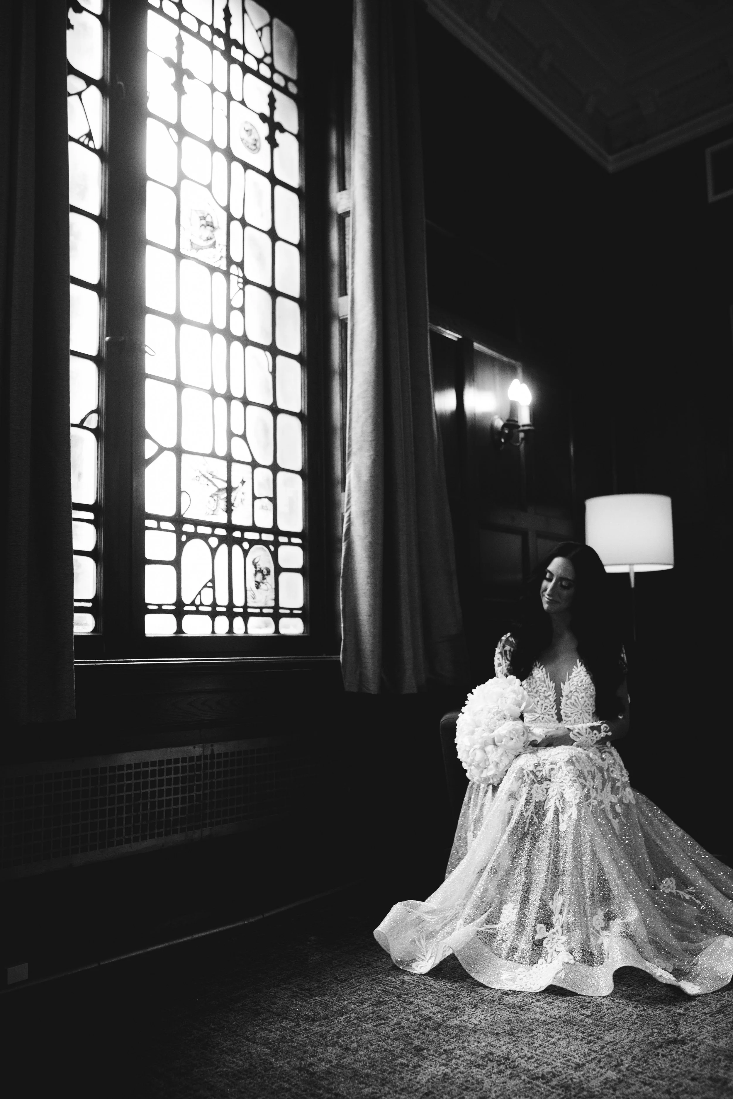 Bride sitting in a chair looking out the window in NYC while wearing her wedding dress