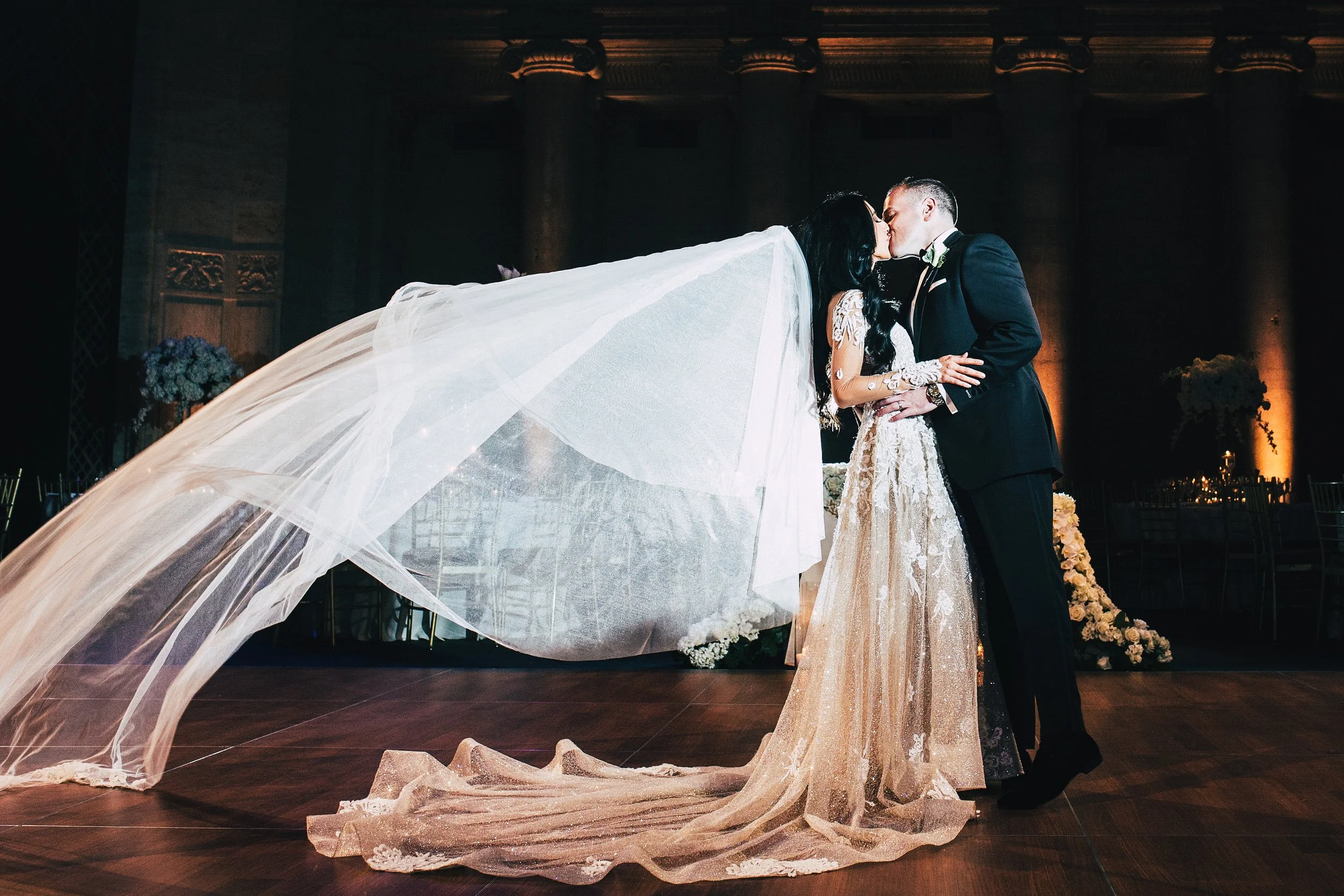 Bride and groom kissing while bride's veil flows in the wind behind her