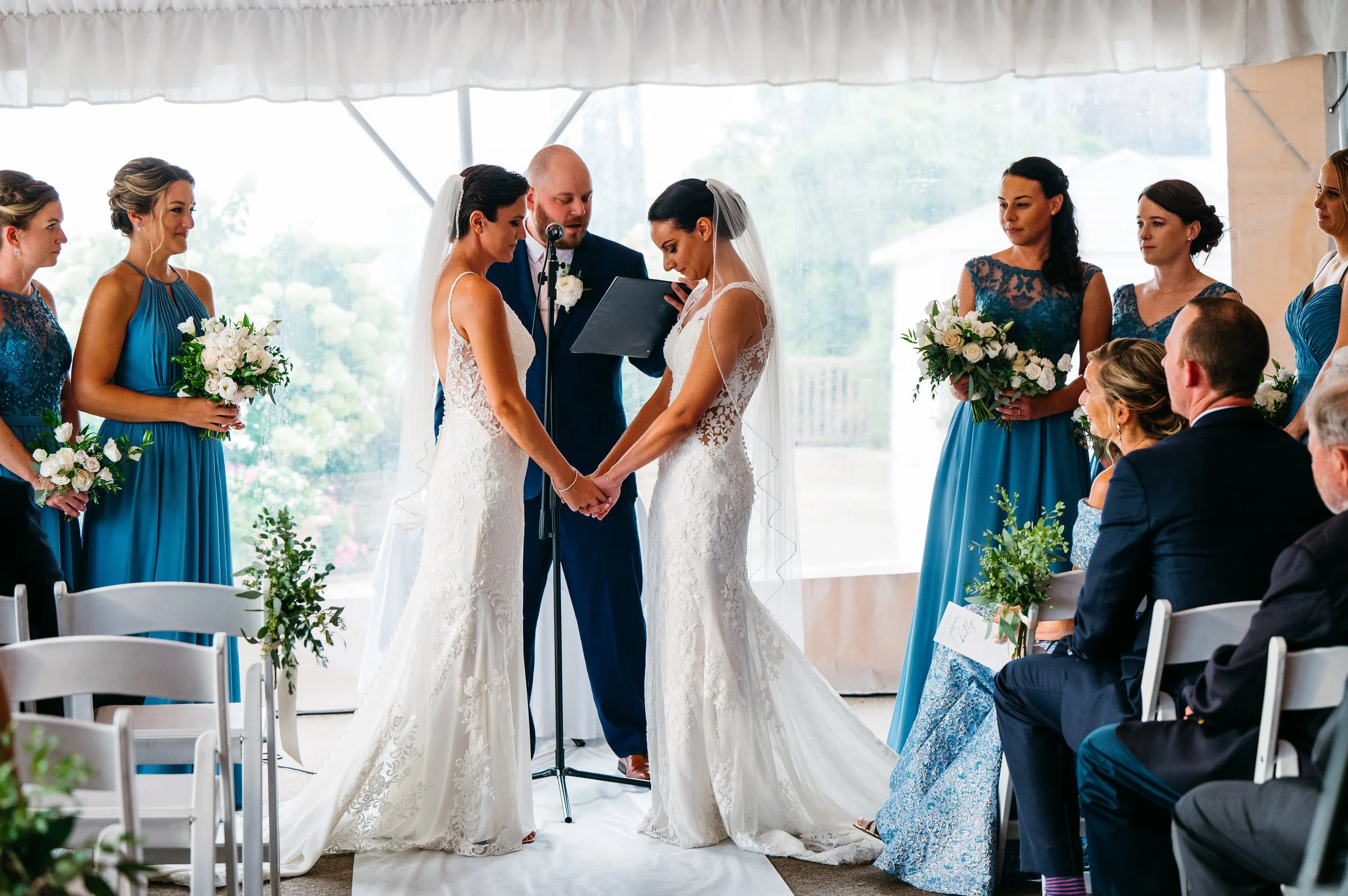 Brides holding hands at the altar at their wedding ceremony under a tent