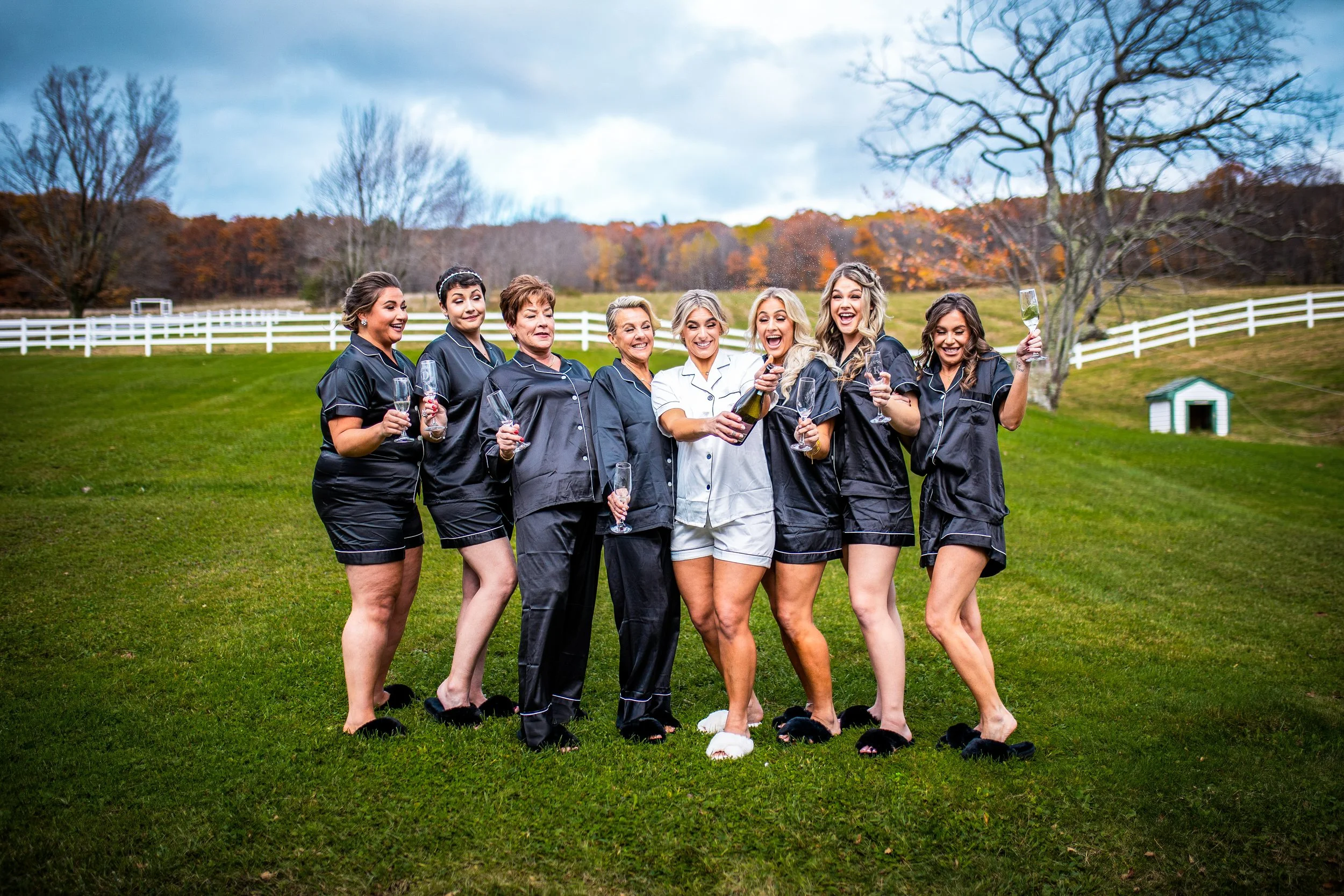Bride and her bridesmaids in matching pajamas on a farm popping a bottle of champagne