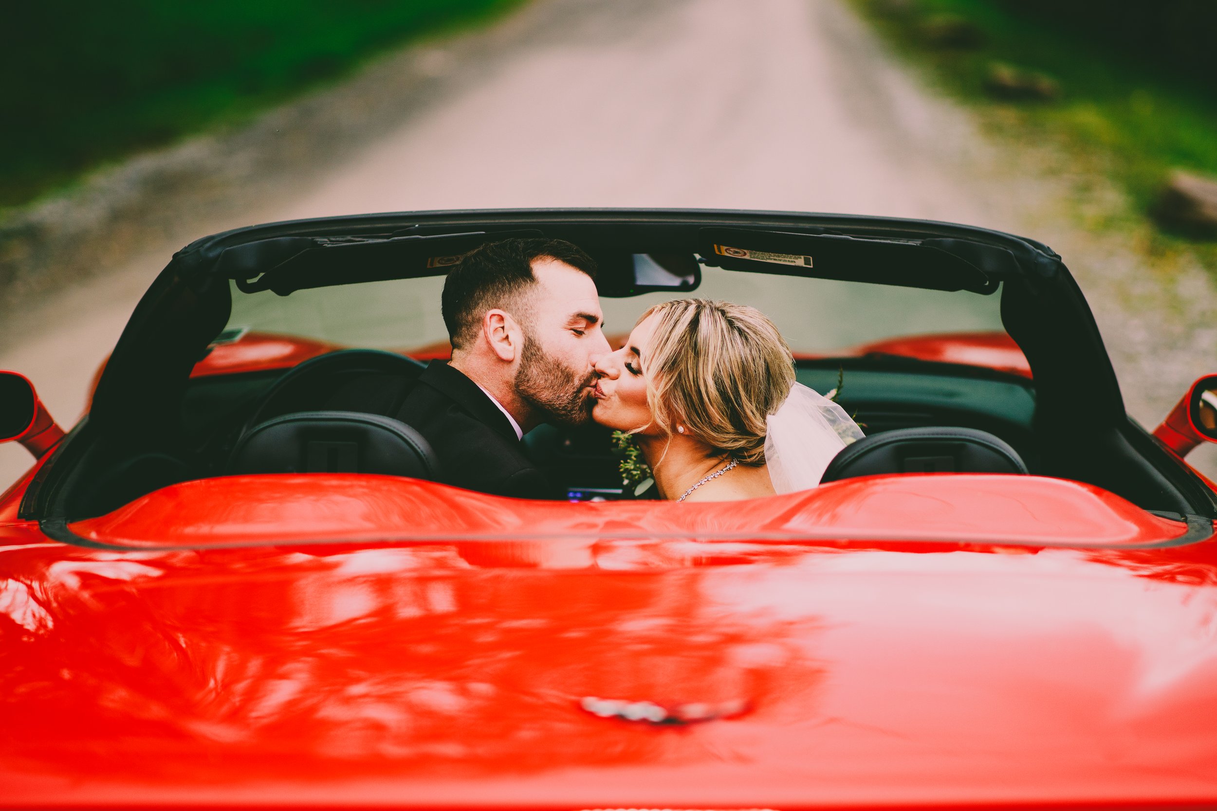 Bride and groom kissing in a red sports car