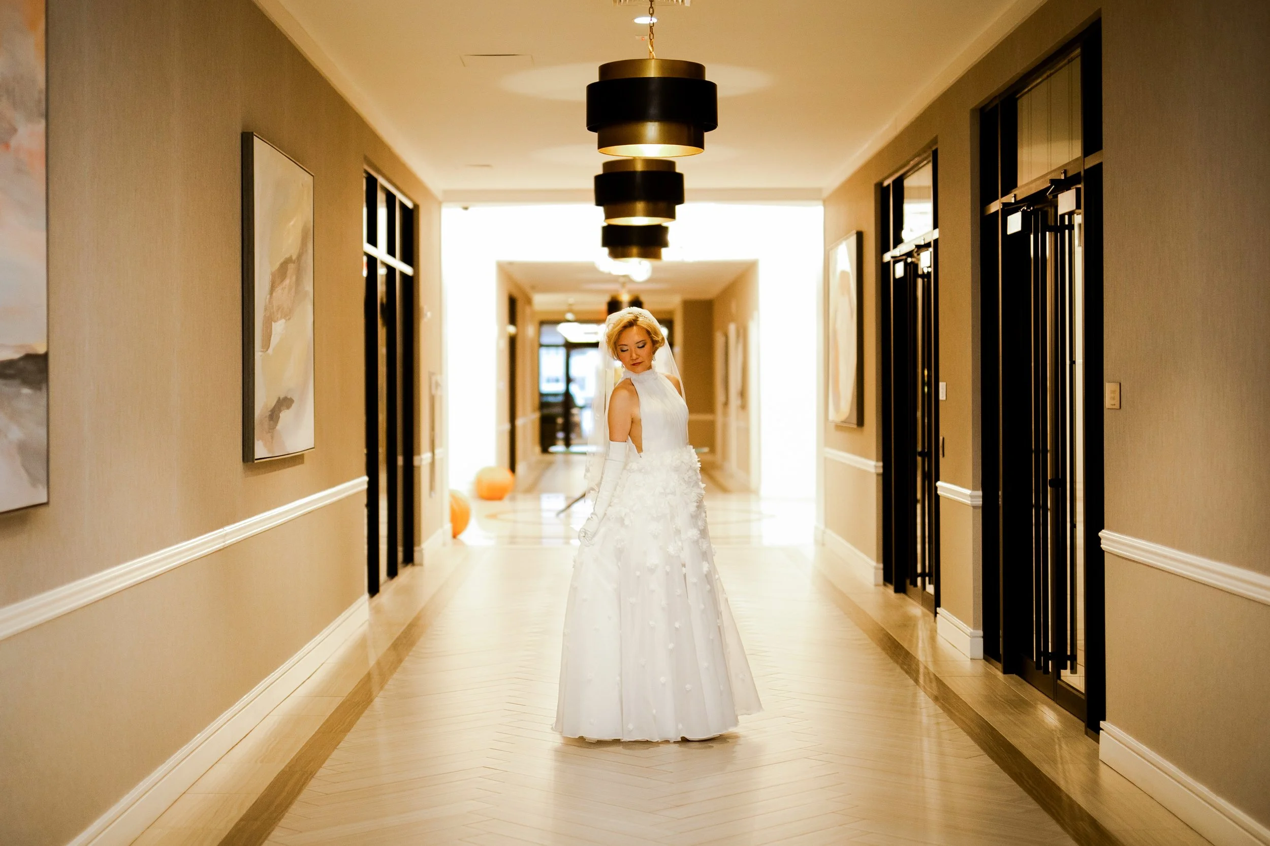Bride posing to show off her dress and veil in an empty hotel hallway