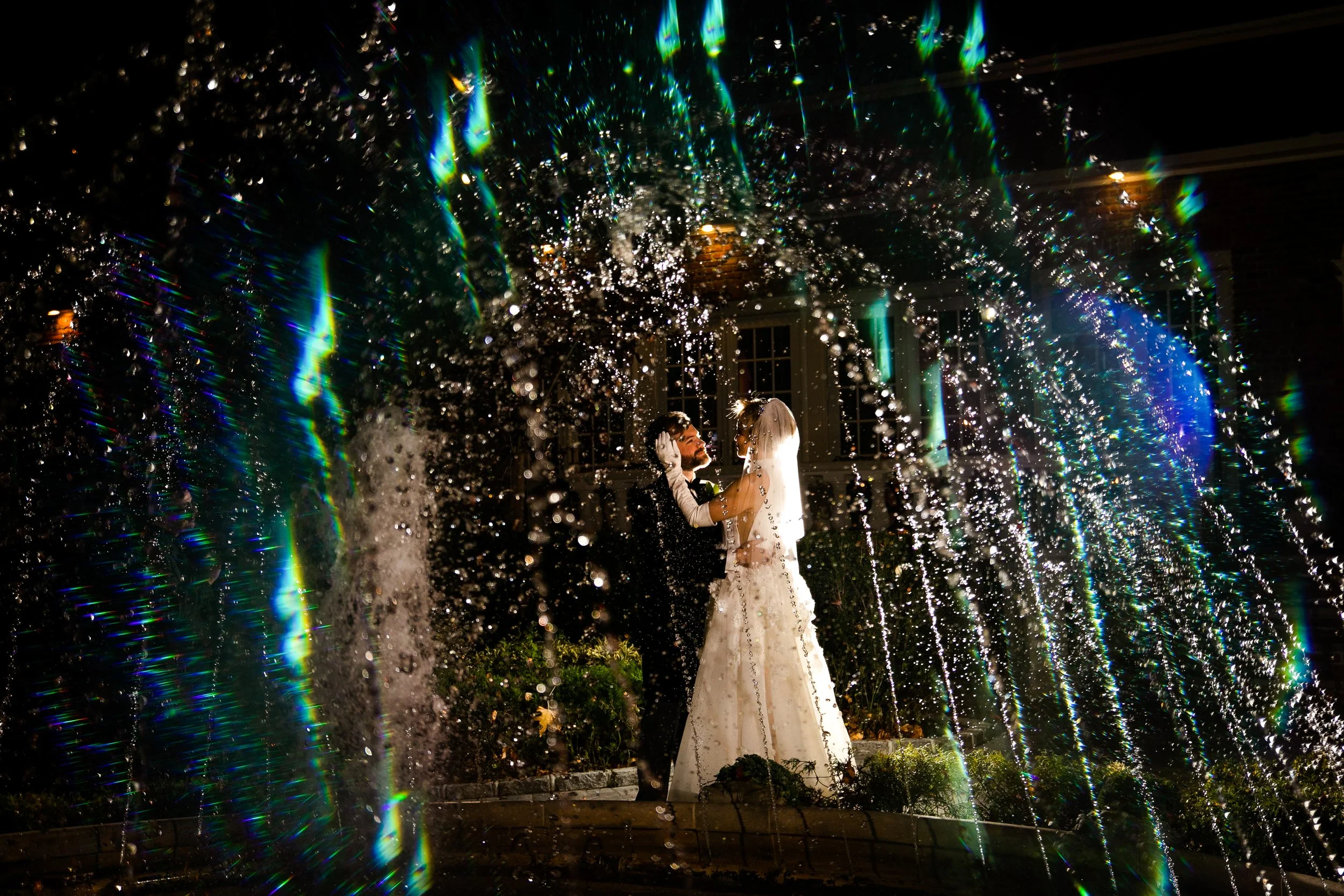 Bride and groom behind a fountain with blue crystal light reflecting on the water
