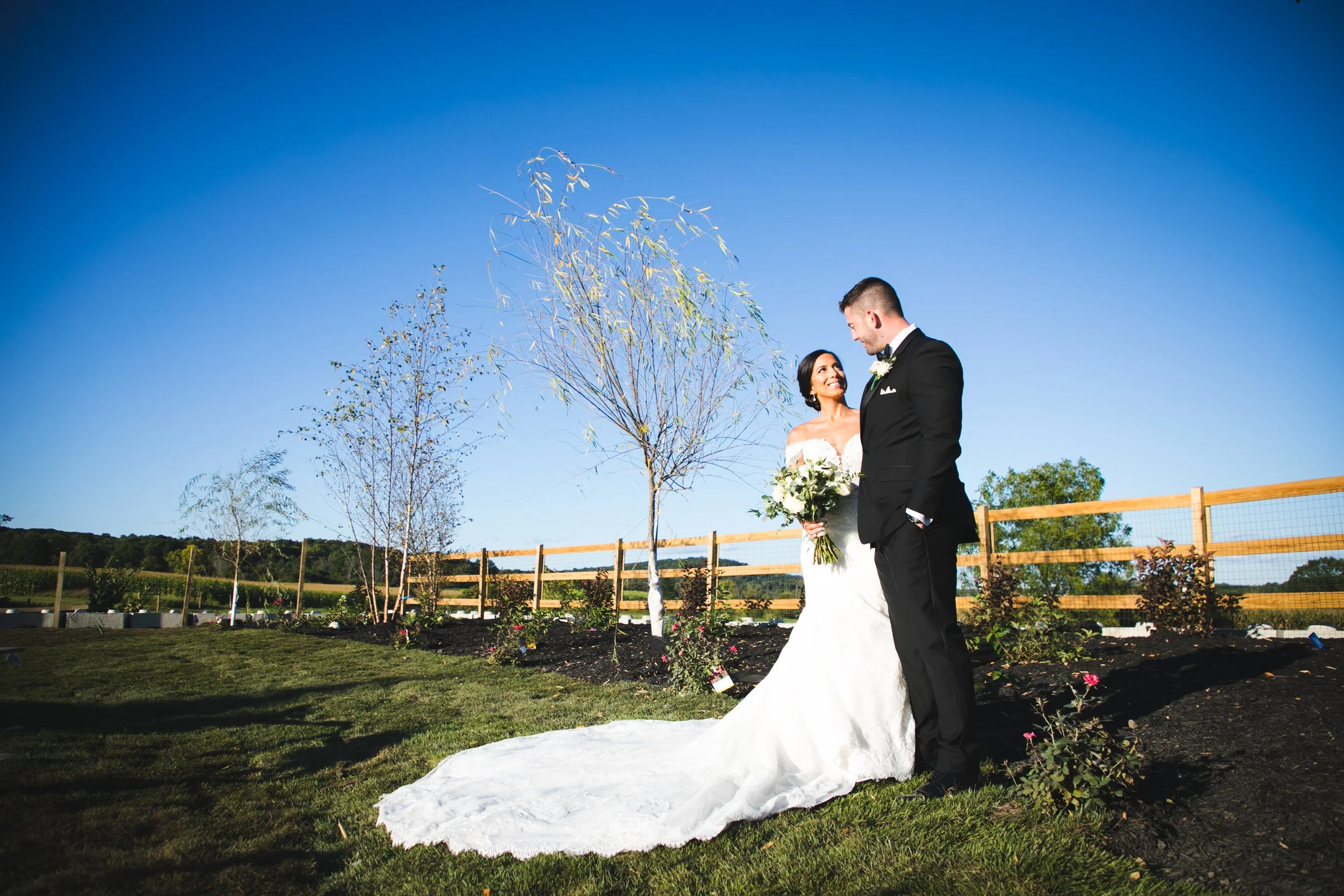 Bride and groom standing in the grass in front of a wooden fence at their rustic barn wedding venue