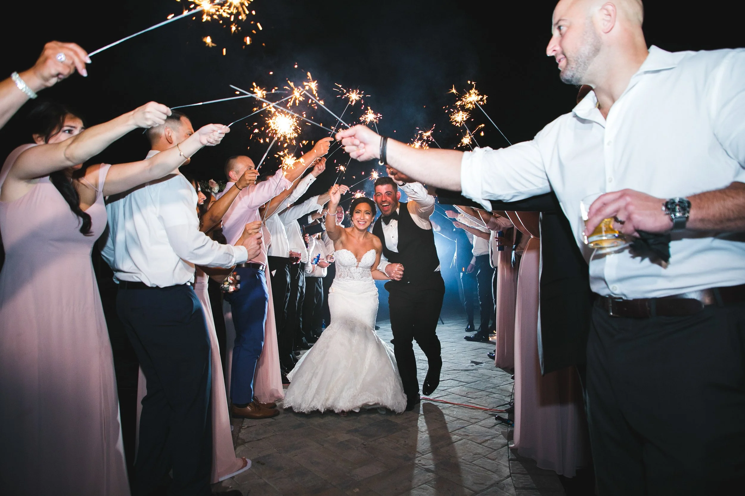 Bride and groom walking under sparklers held by their bridesmaids and groomsmen lined up around them