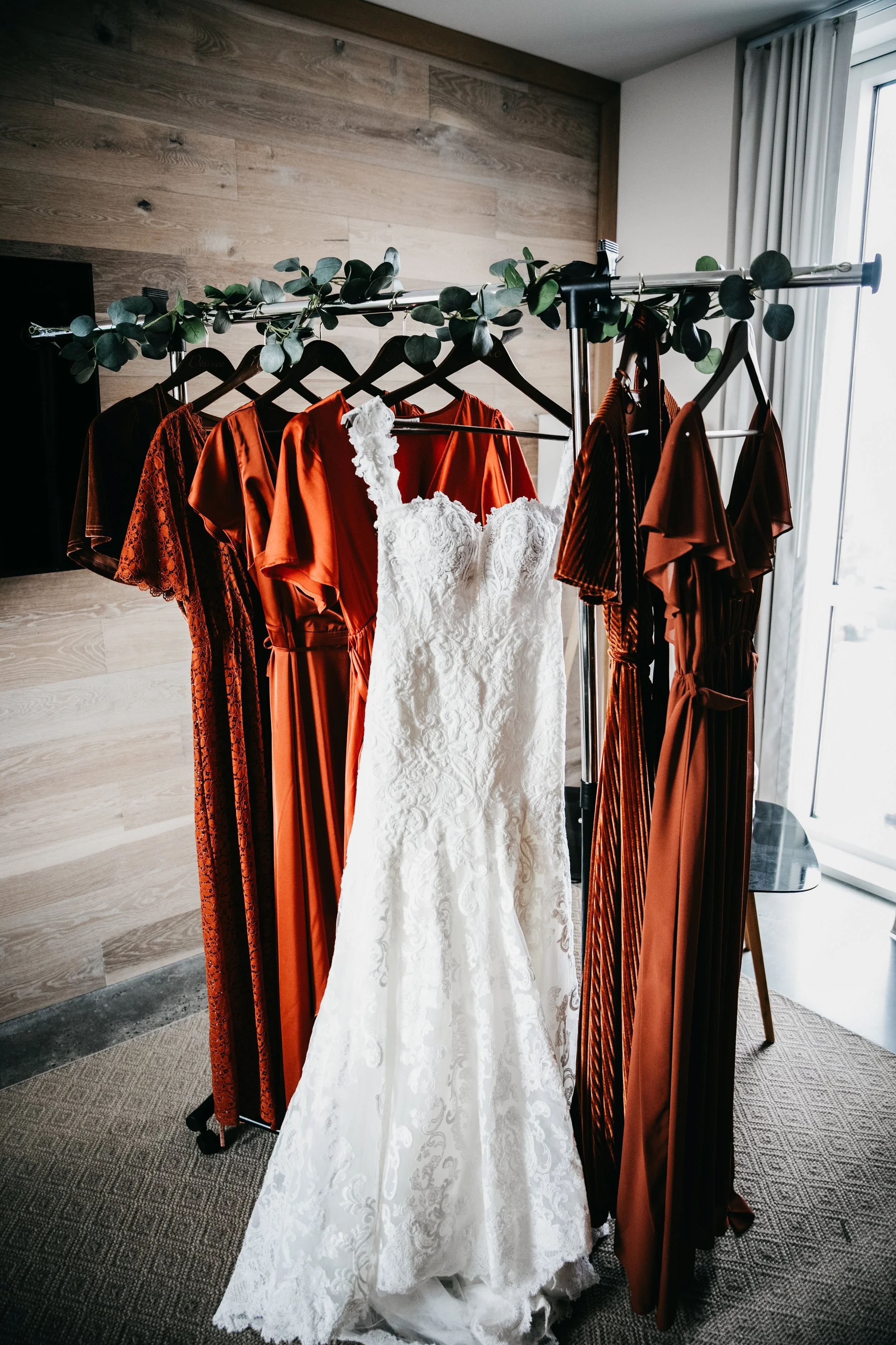 Wedding dress and orange and red bridesmaids dresses hanging on a rack