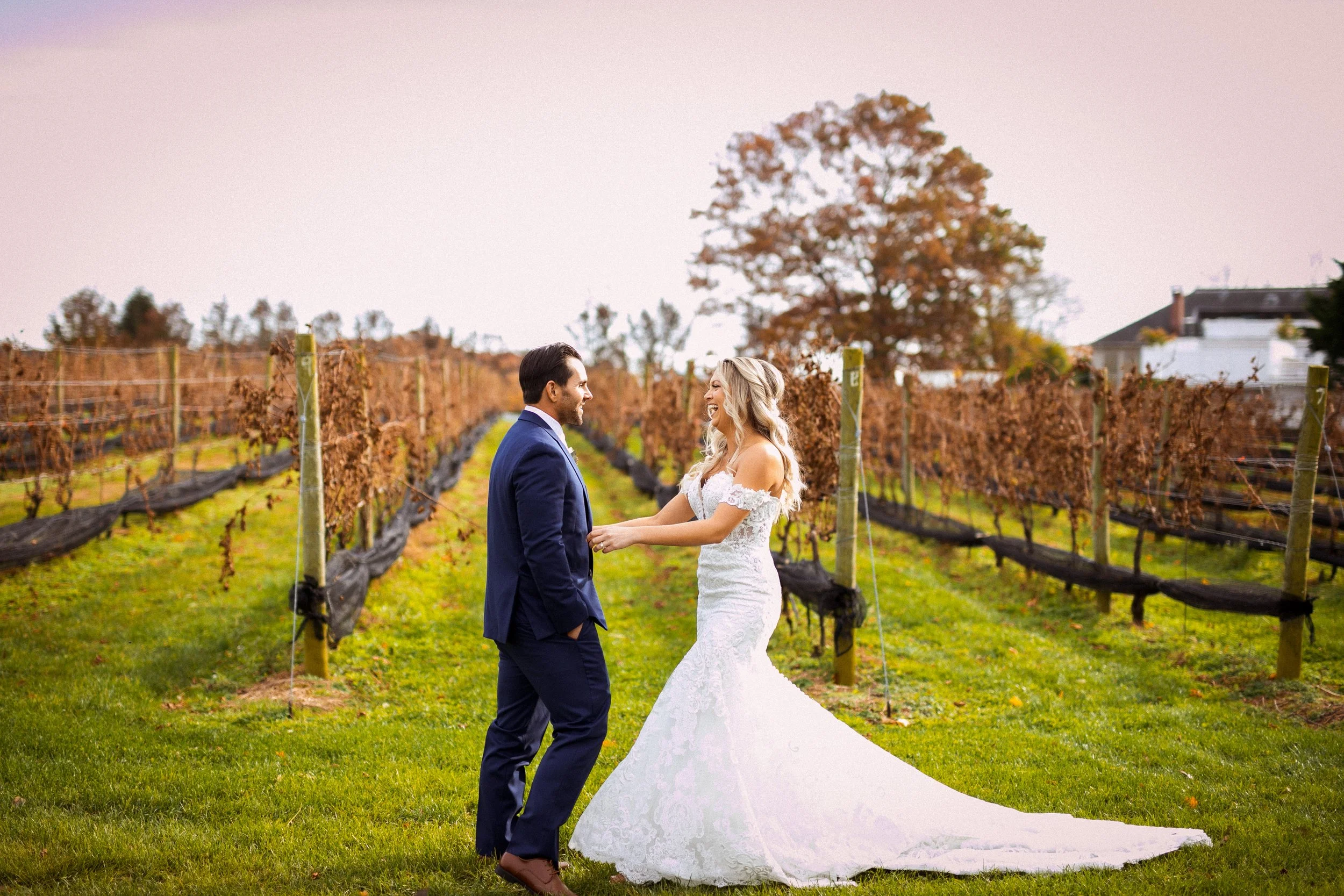 Bride reaching out her arms to her groom for a hug during their first look outside in front of a vineyard in the fall