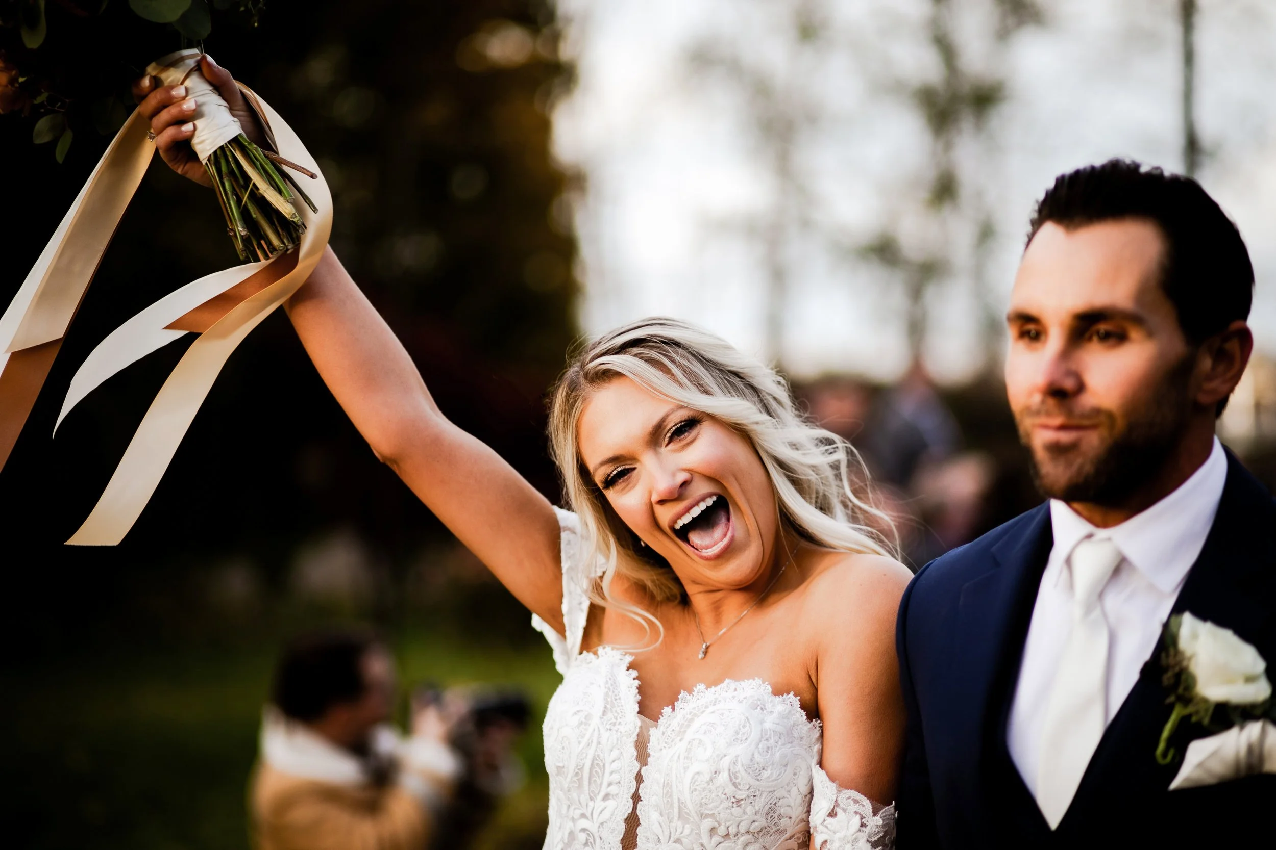 close up of bride cheering and holding up her bouquet while walking back down the aisle with her new husband after their wedding ceremony
