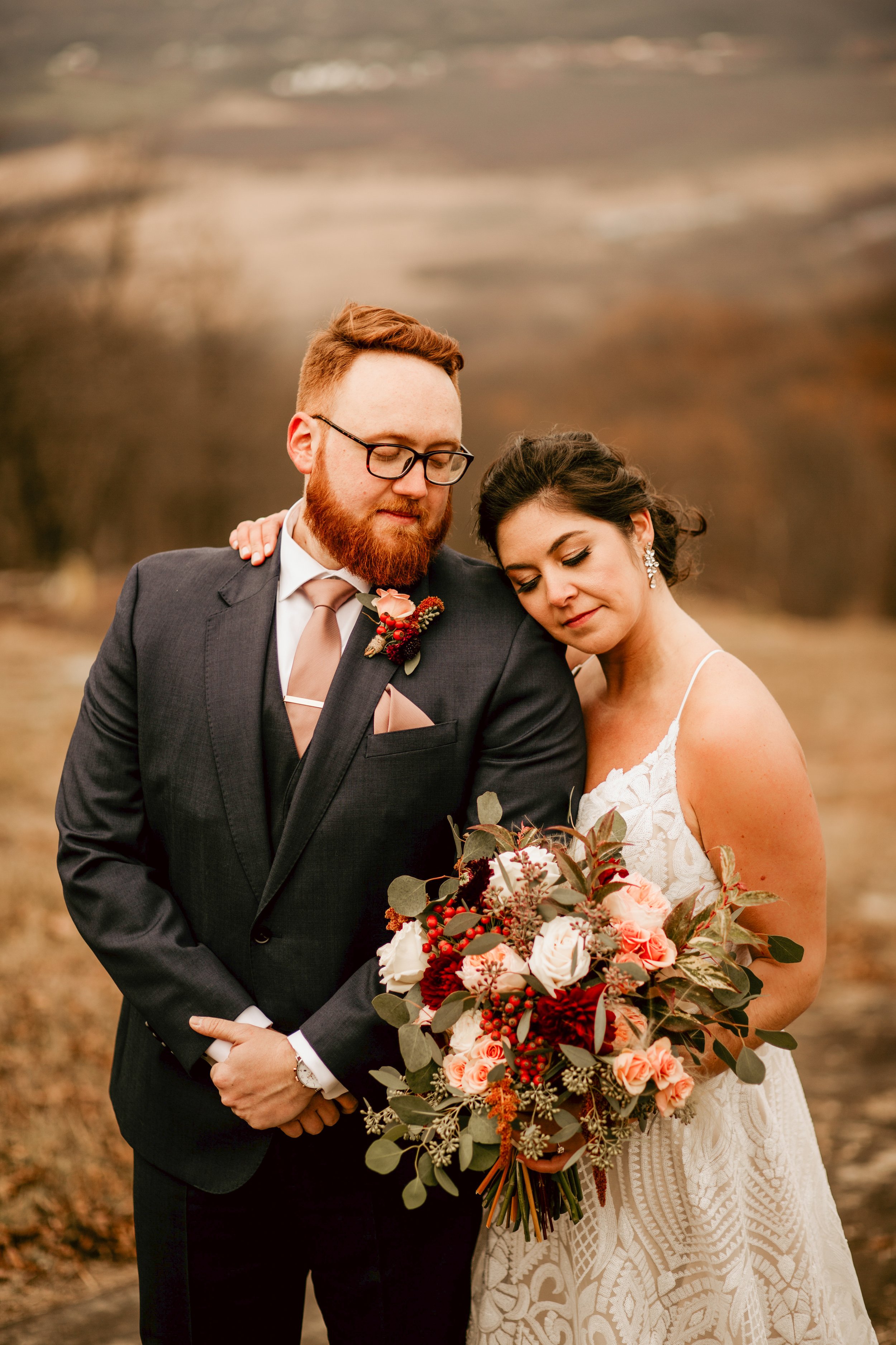 Bride resting her head on her groom's shoulder while she holds her wedding flower bouquet at a mountain wedding venue in New Jersey