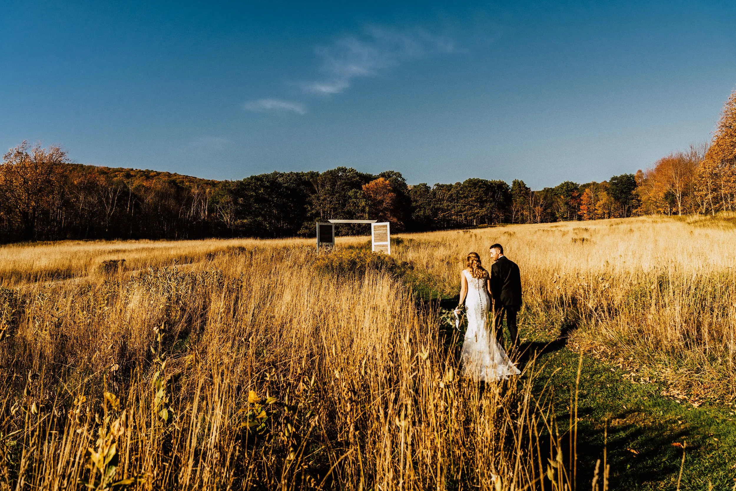 Bride and groom walking away through a wheat field towards their ceremony arch on a sunny fall day
