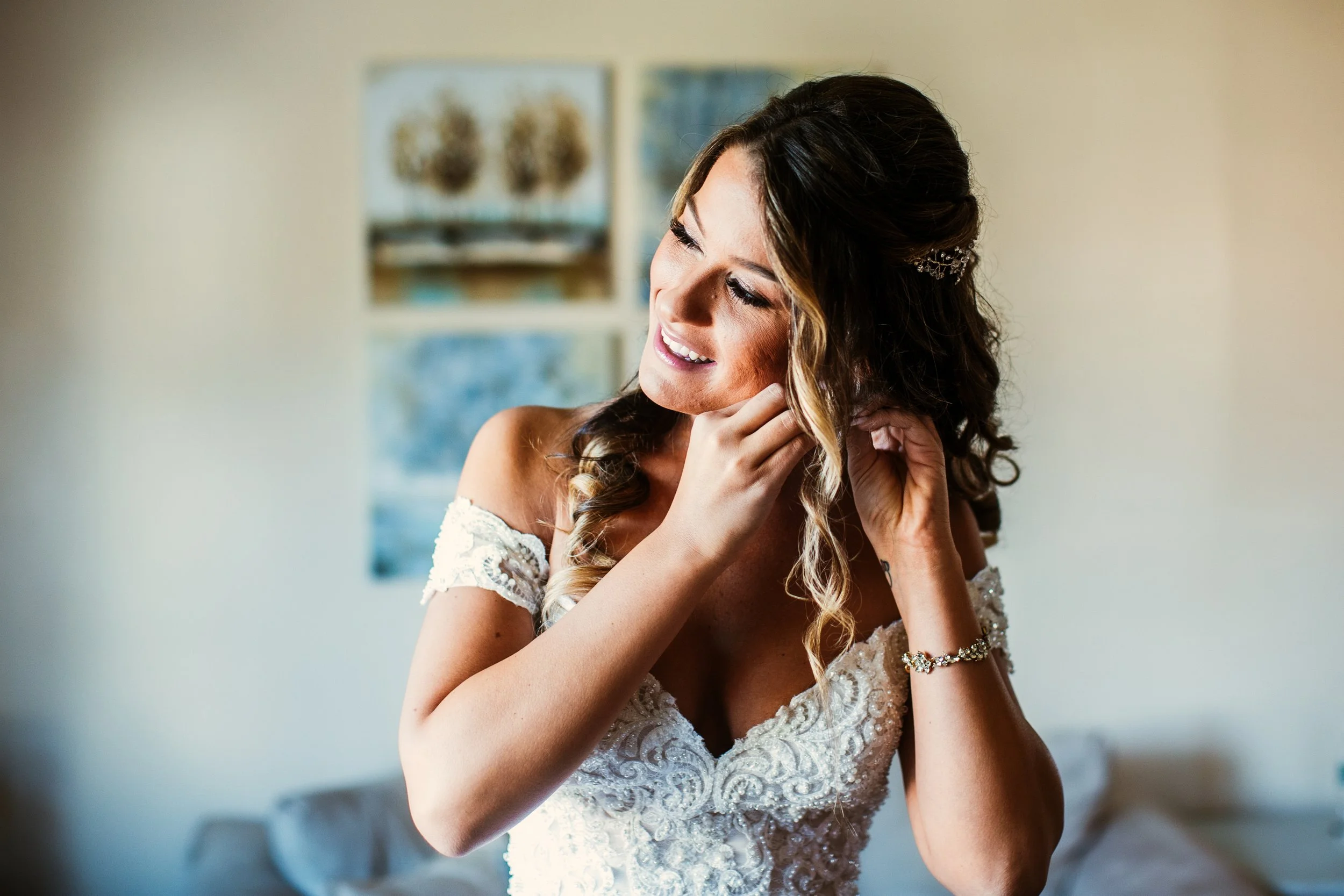 Bride putting on her earrings while wearing her wedding dress at home