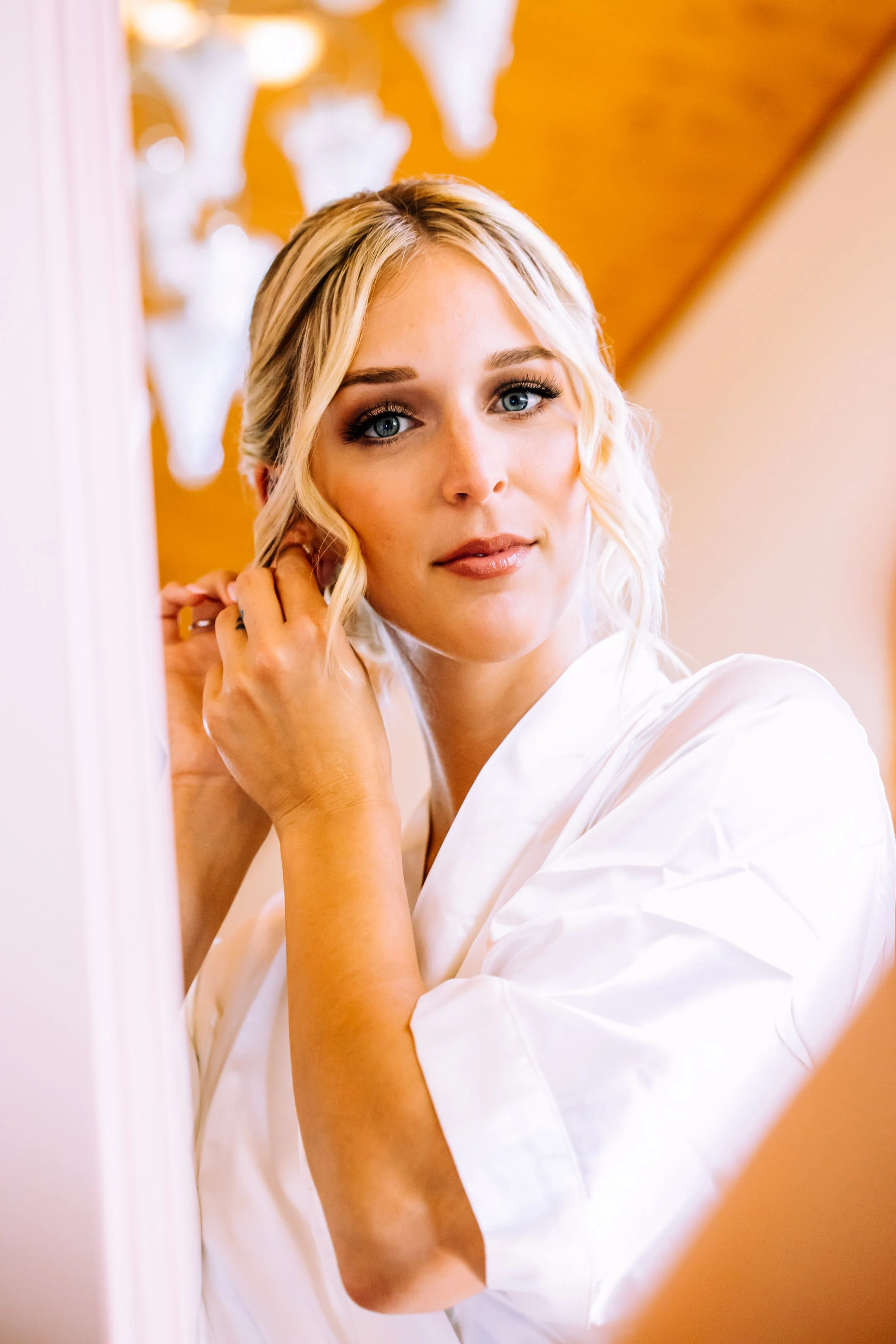 Bride putting on her earring in her white robe before the wedding