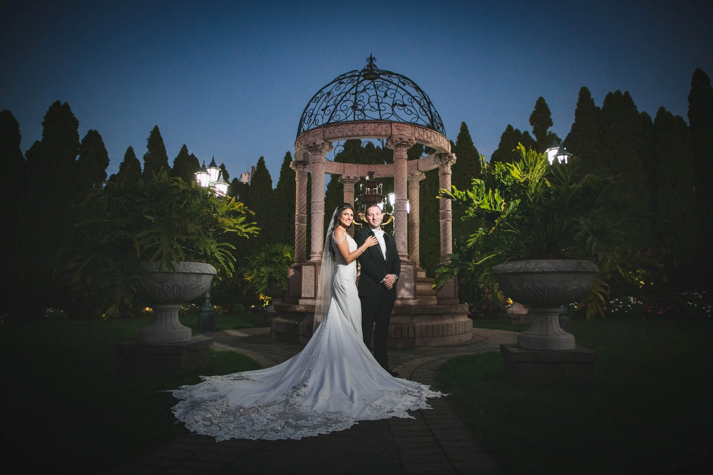 Bride and groom standing in front of a gazebo at night with spotlight shining on them