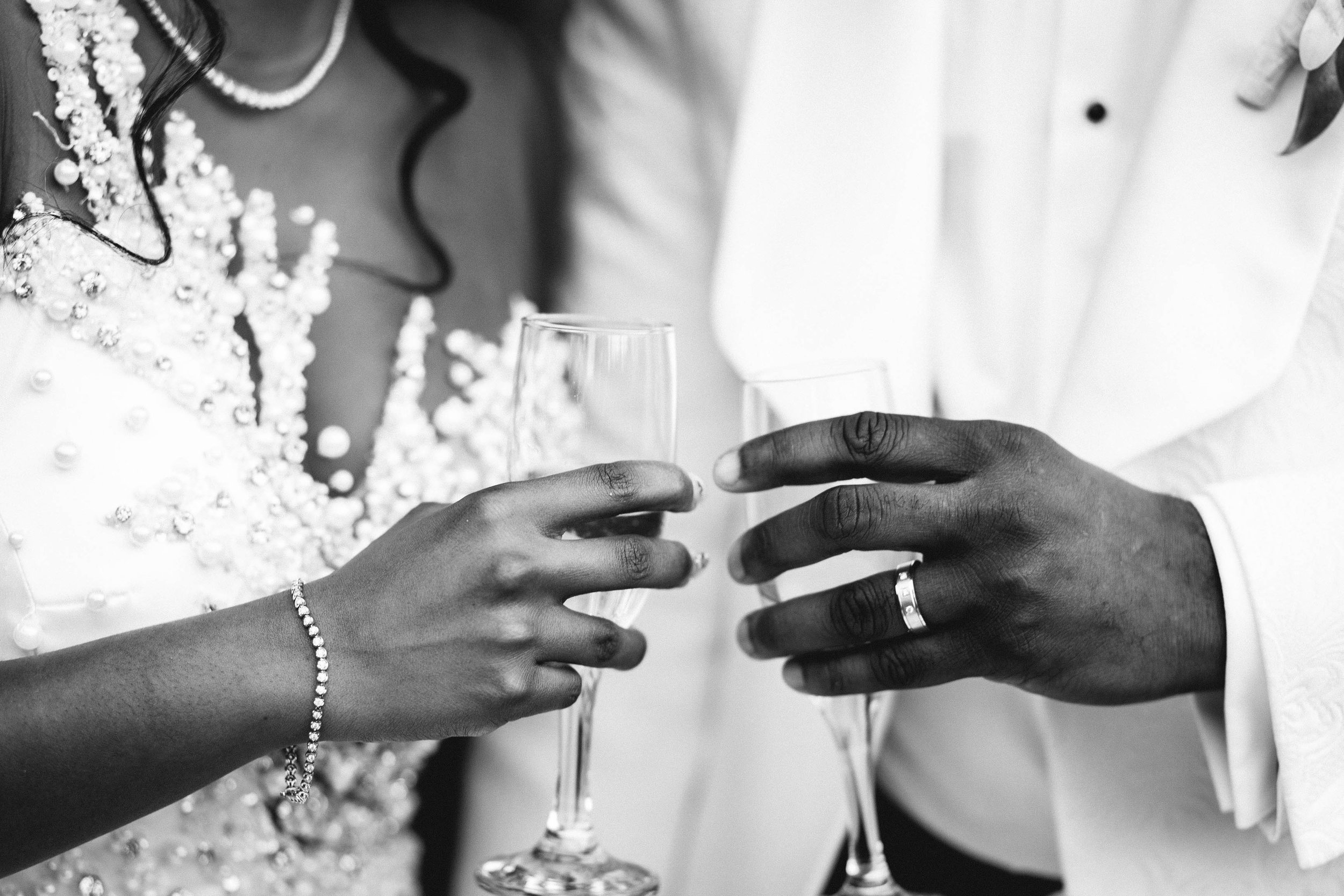 Close up photography of bride and groom clinking champagne glasses and showing off wedding ring