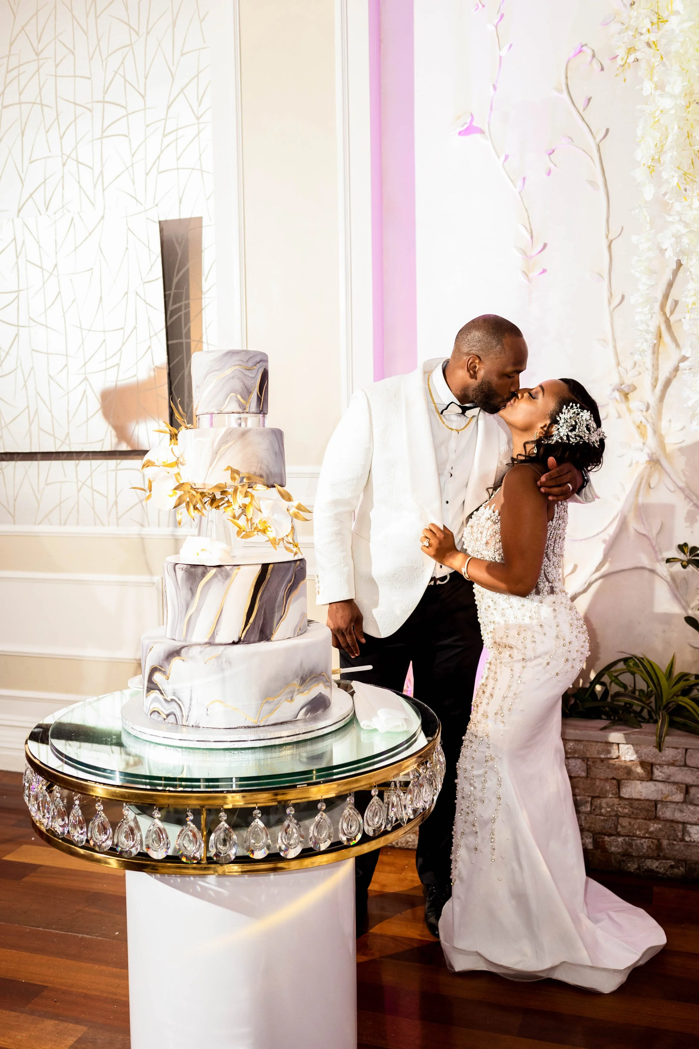 Bride and groom kissing behind their black and white marble wedding cake with gold accents