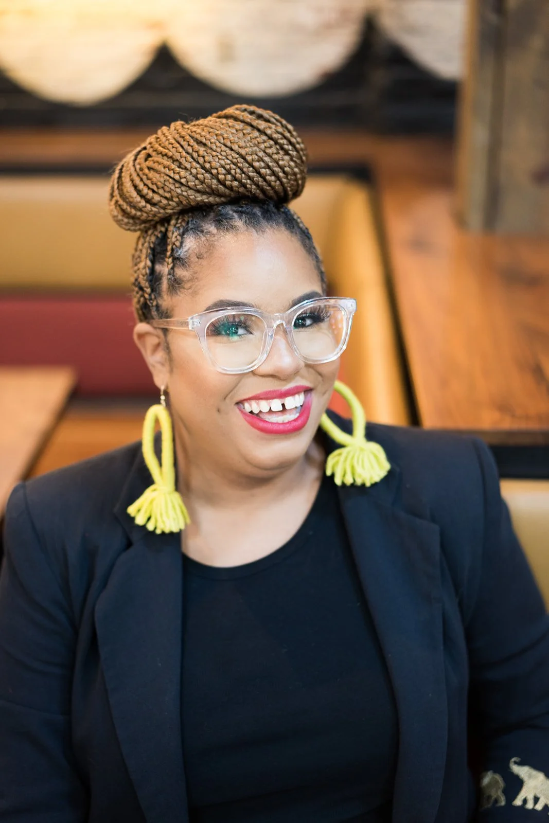 Close-up of woman with clear eyeglasses and bright yellow statement earrings smiling wearing black blazer