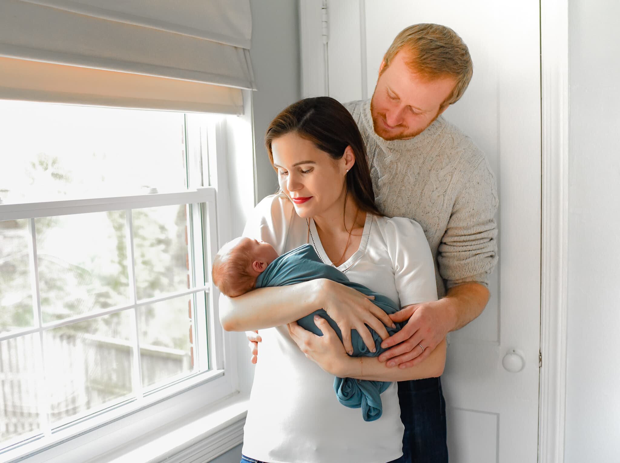 Silver Spring Maryland Newborn Photoshoot - mom and dad cradling baby by window