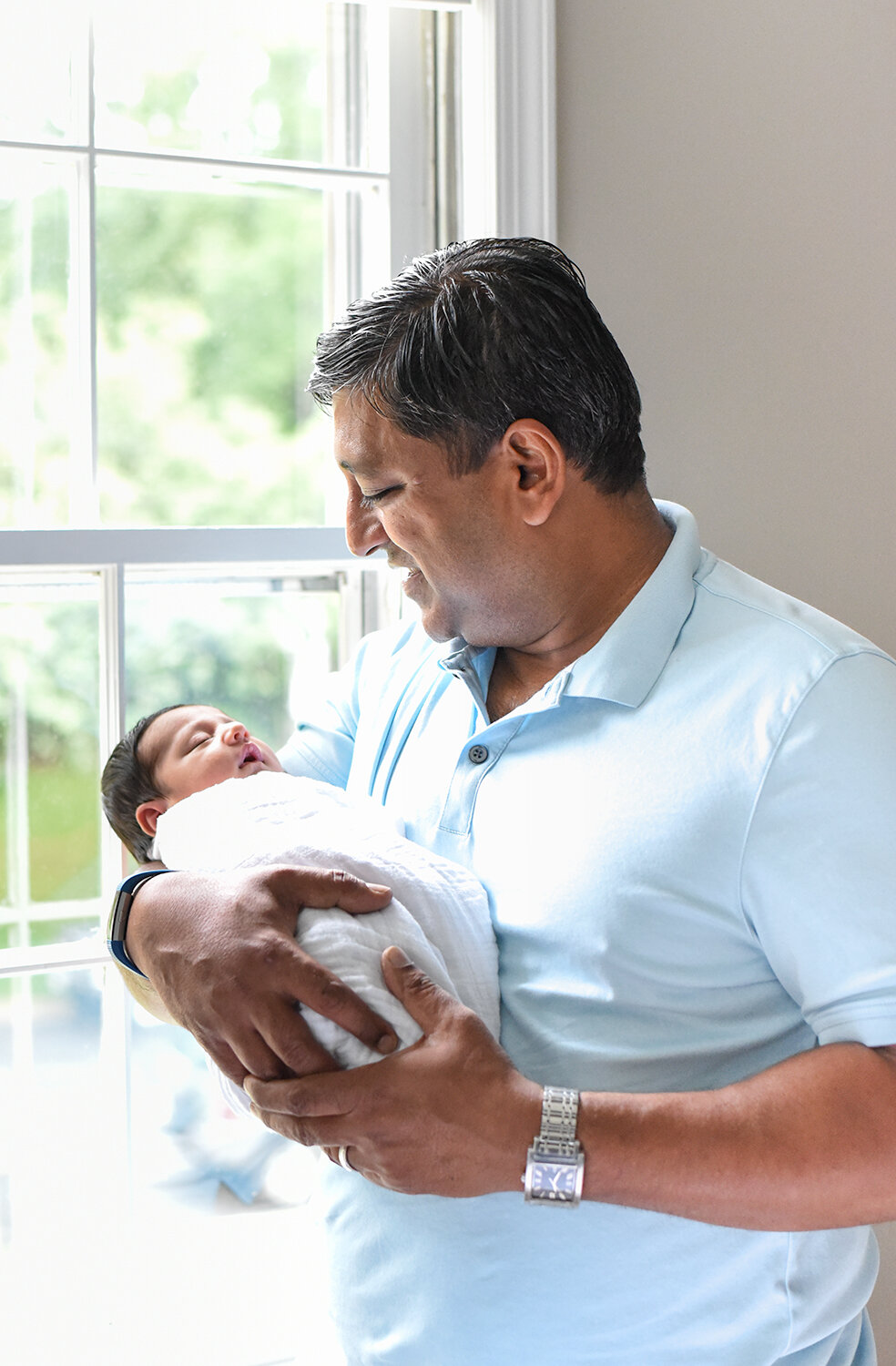 Maryland Newborn Photographer - dad cradling baby in front of the window