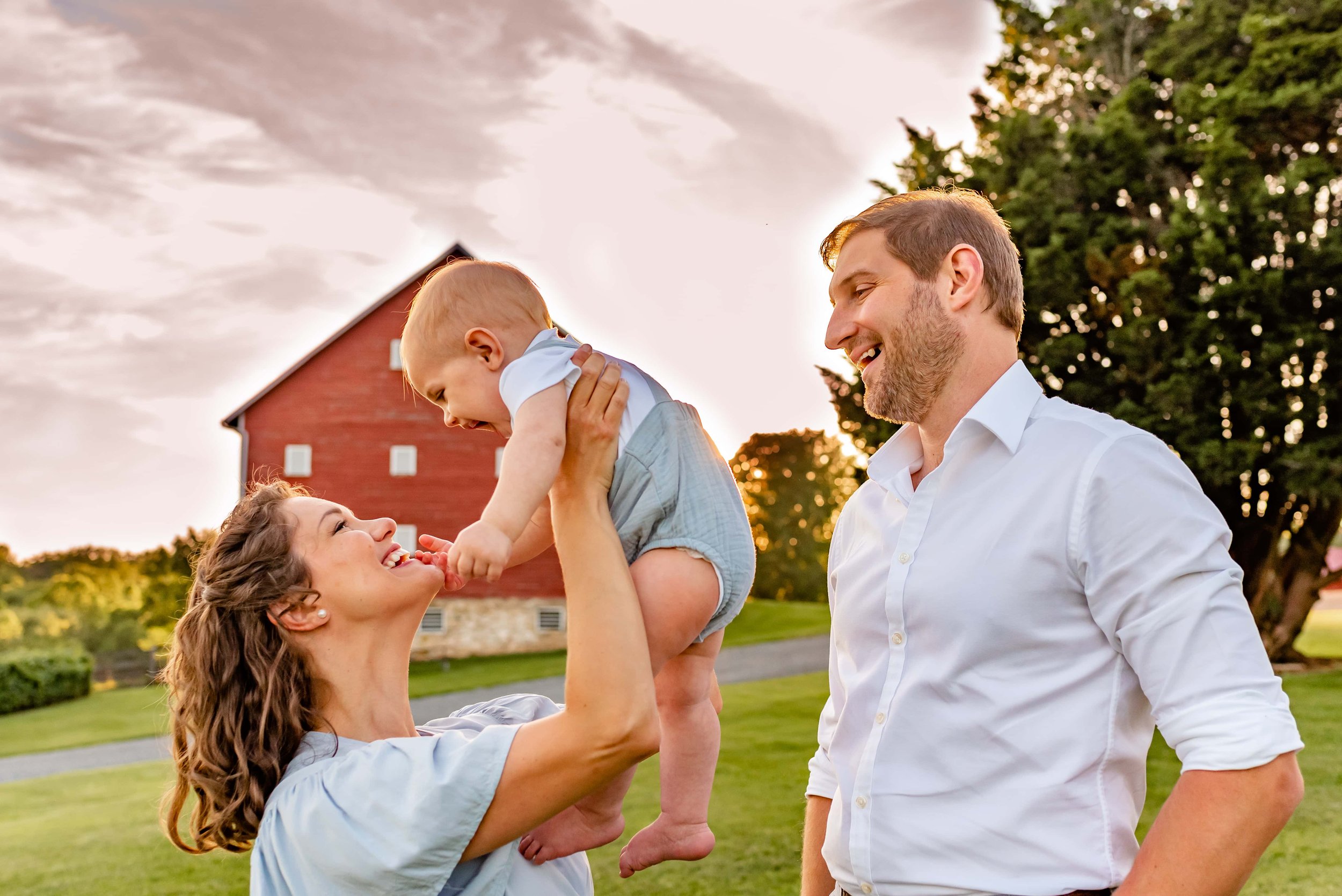 Maryland mom, dad and baby playing in front of barn