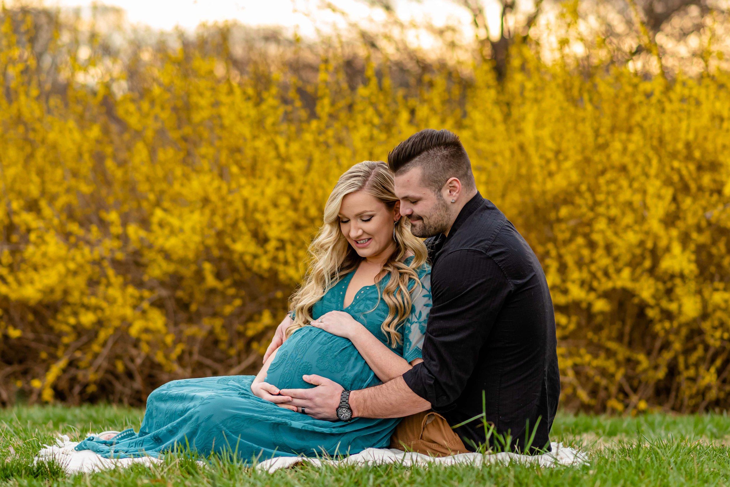 Maryland Maternity Photoshoot with expecting couple sitting on a blanket looking down at belly