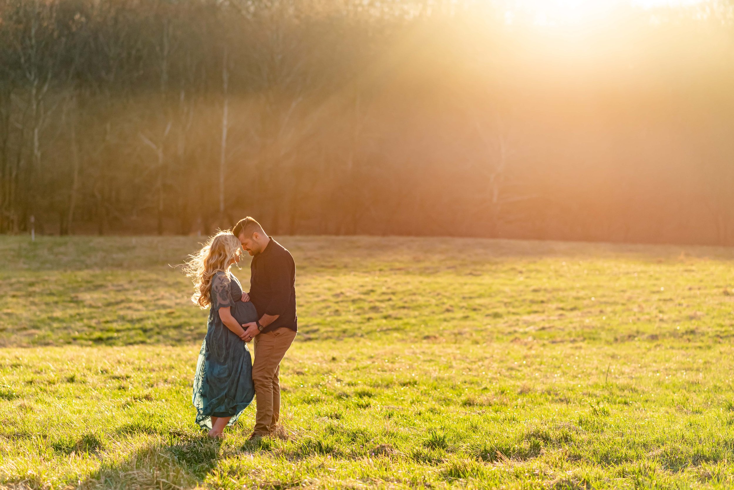 Maryland Maternity photo of couple standing forehead to forehead in a field surrounded by sunbeams