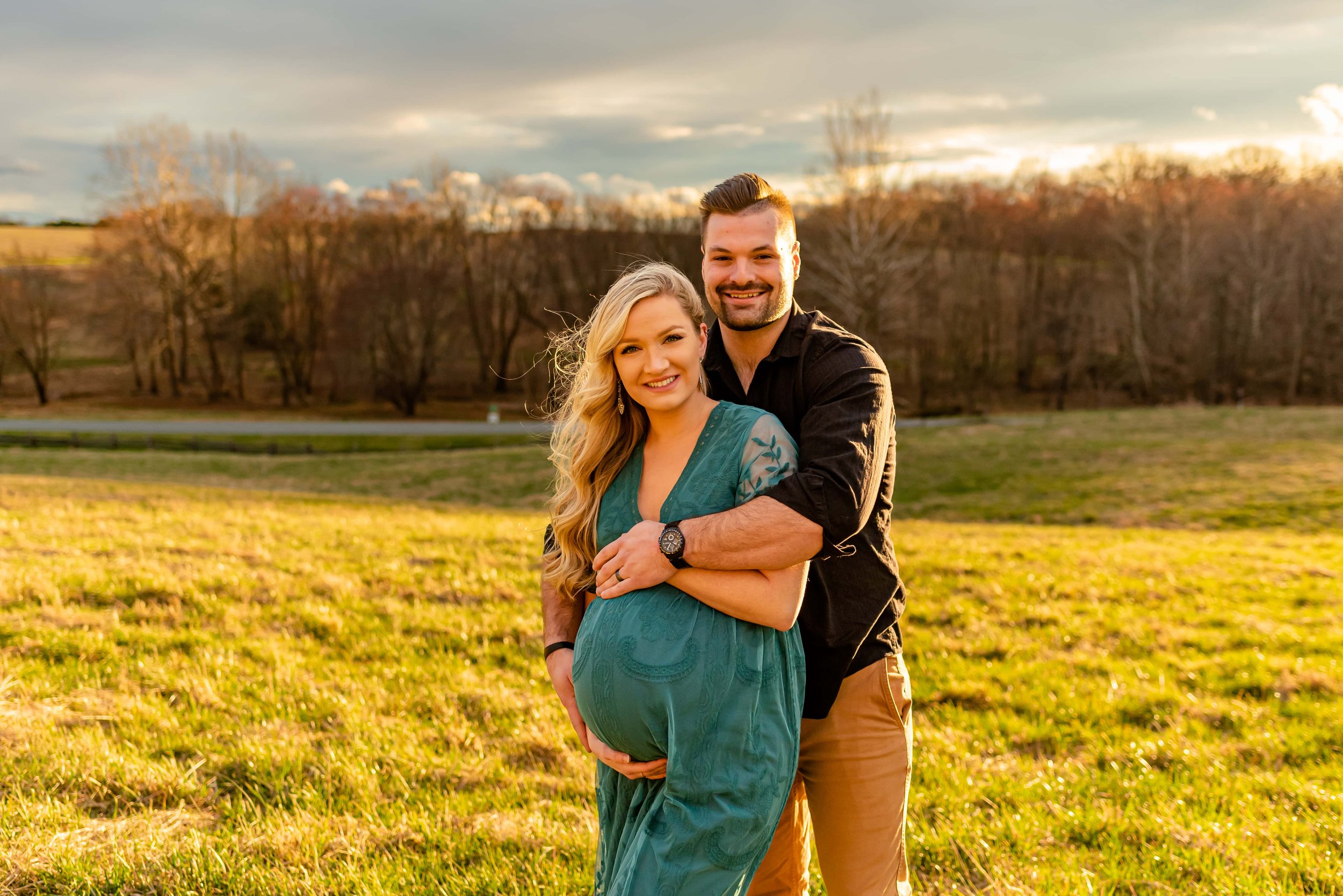 Maternity photos with couple standing in a field smiling at the camera
