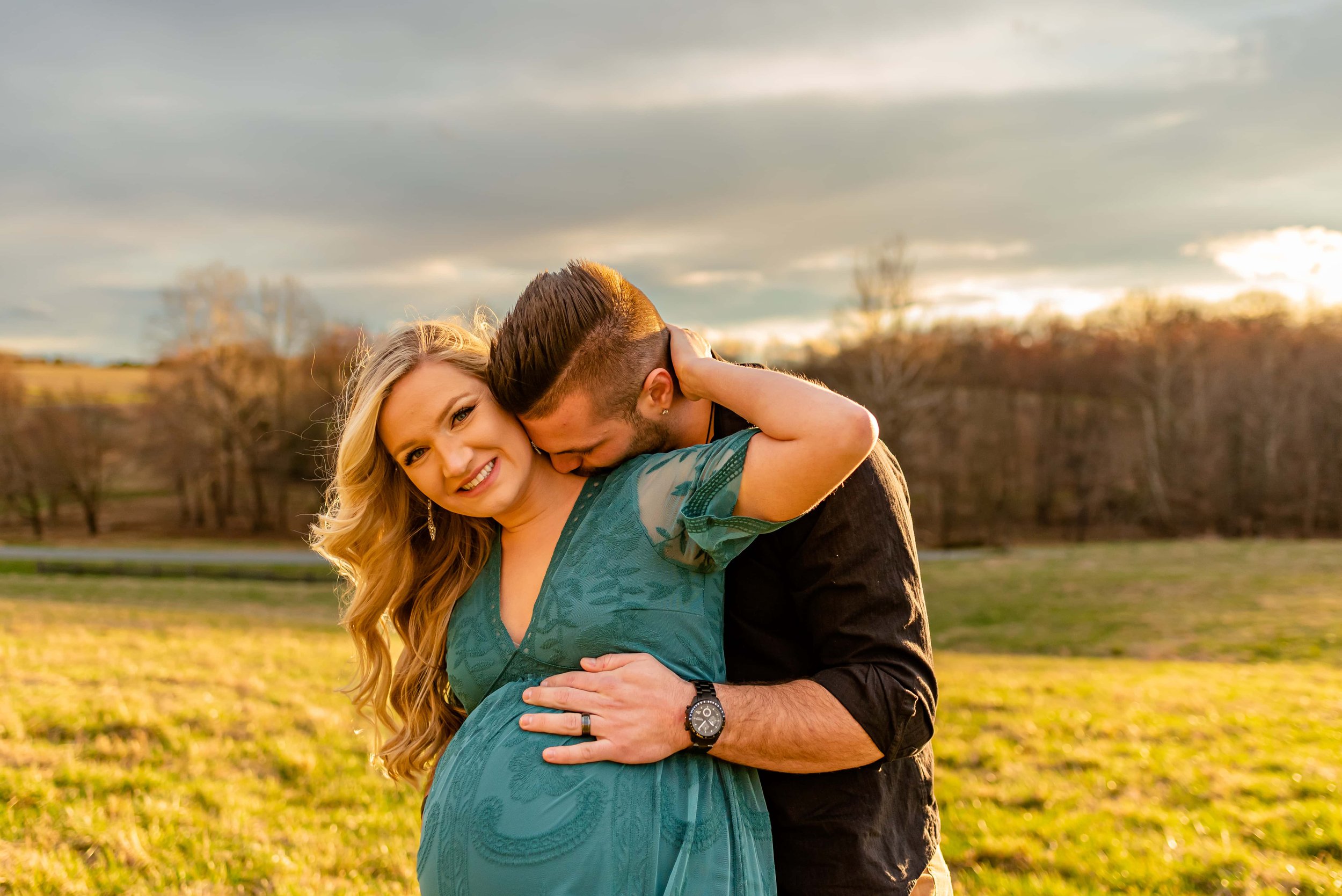 Maternity photos with couple standing in a field cuddling
