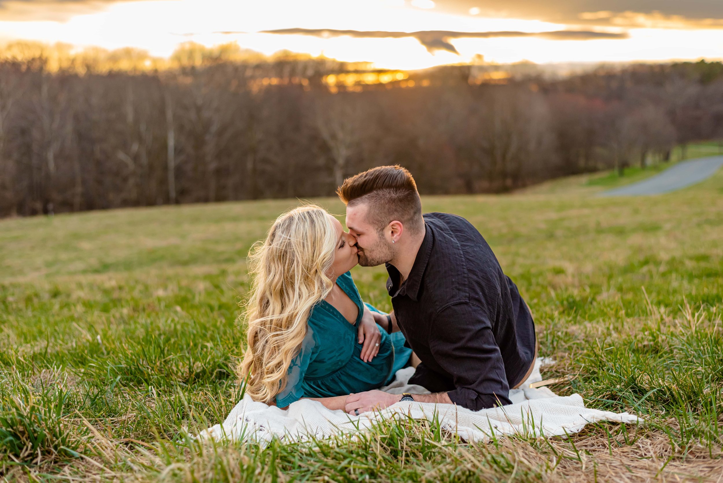 Maternity photos with couple laying on a blanket in a field and kissing