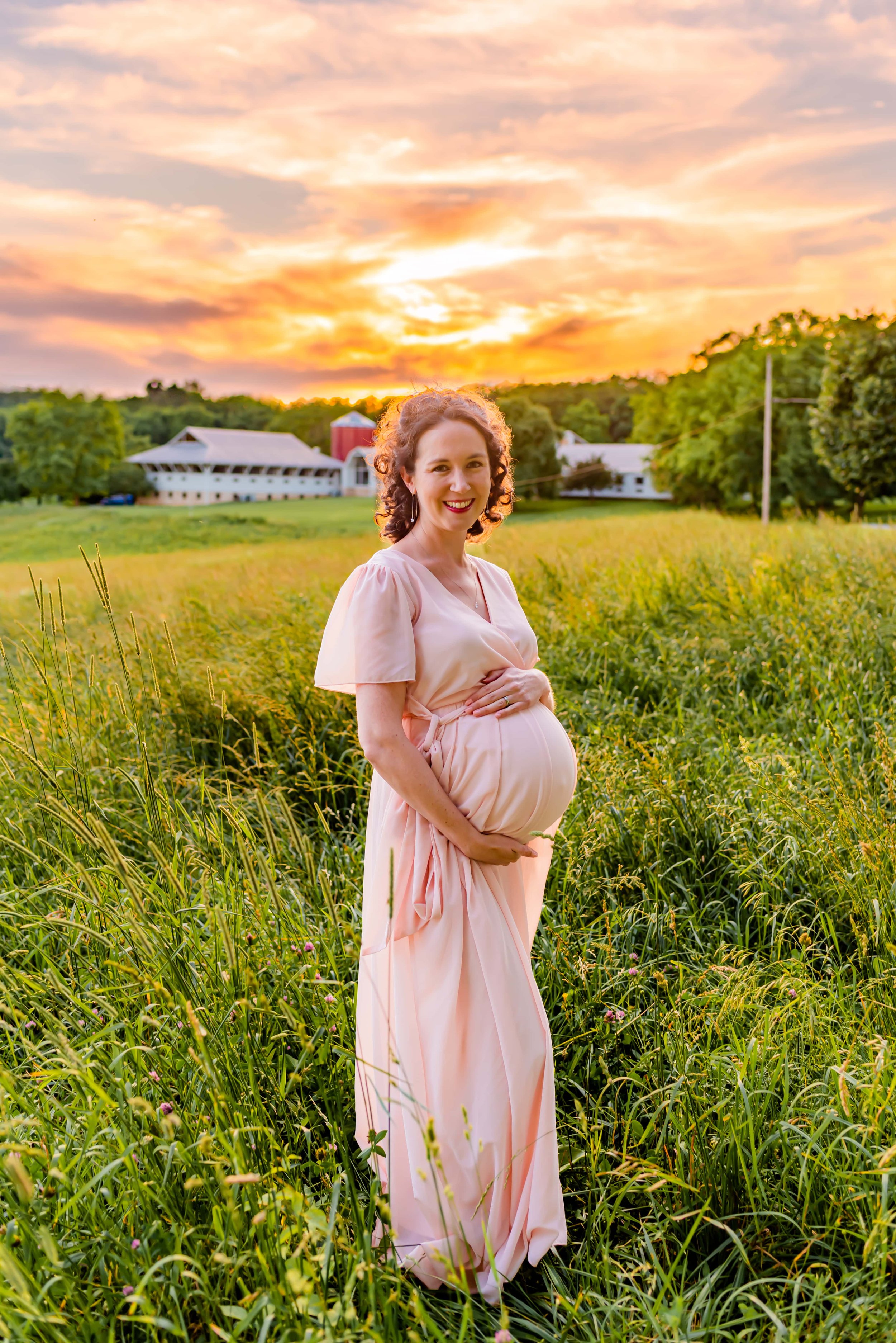 Maternity photo of woman standing in a field smiling at the camera at sunset