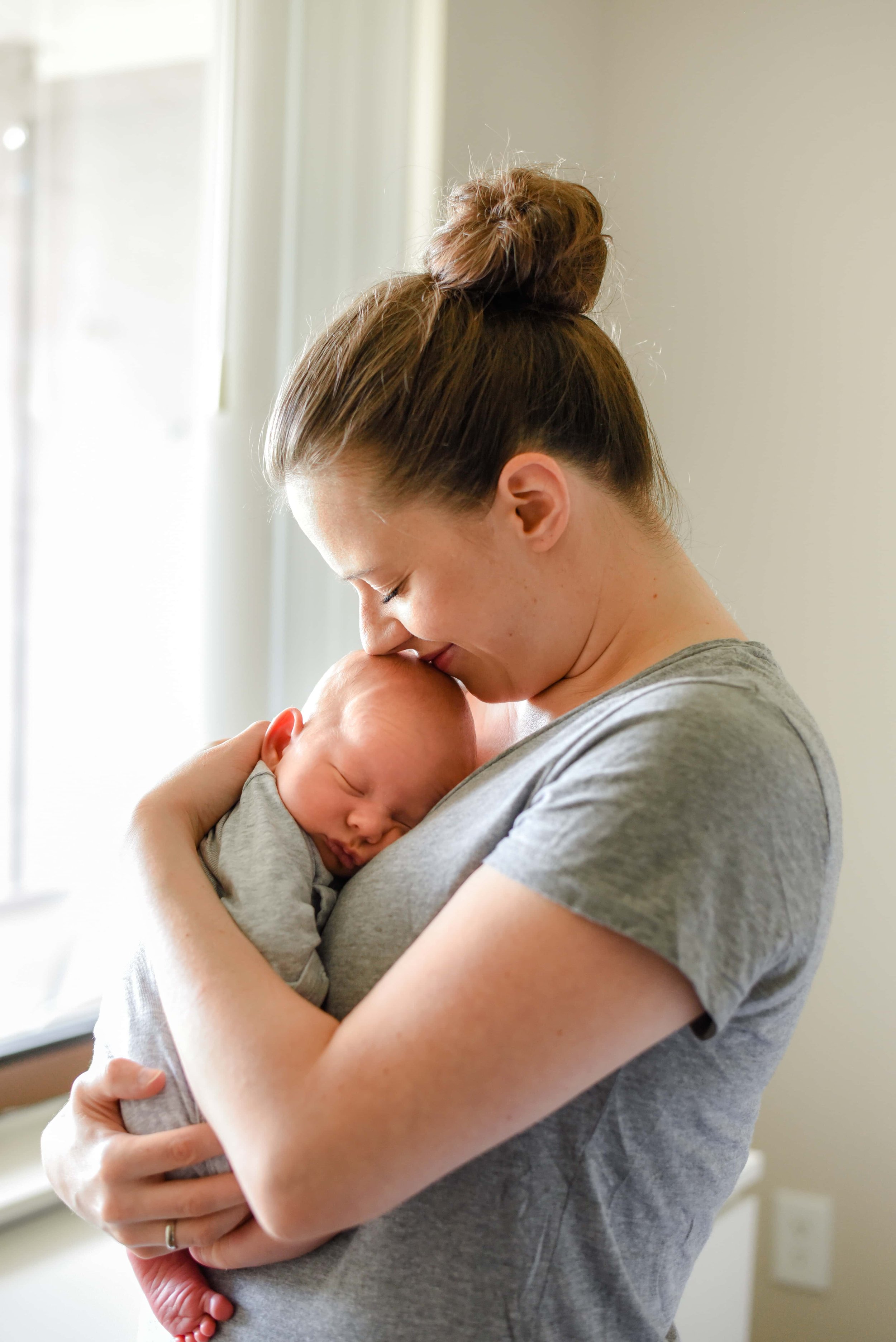 Natural newborn photograph of mom and baby cuddling by the window