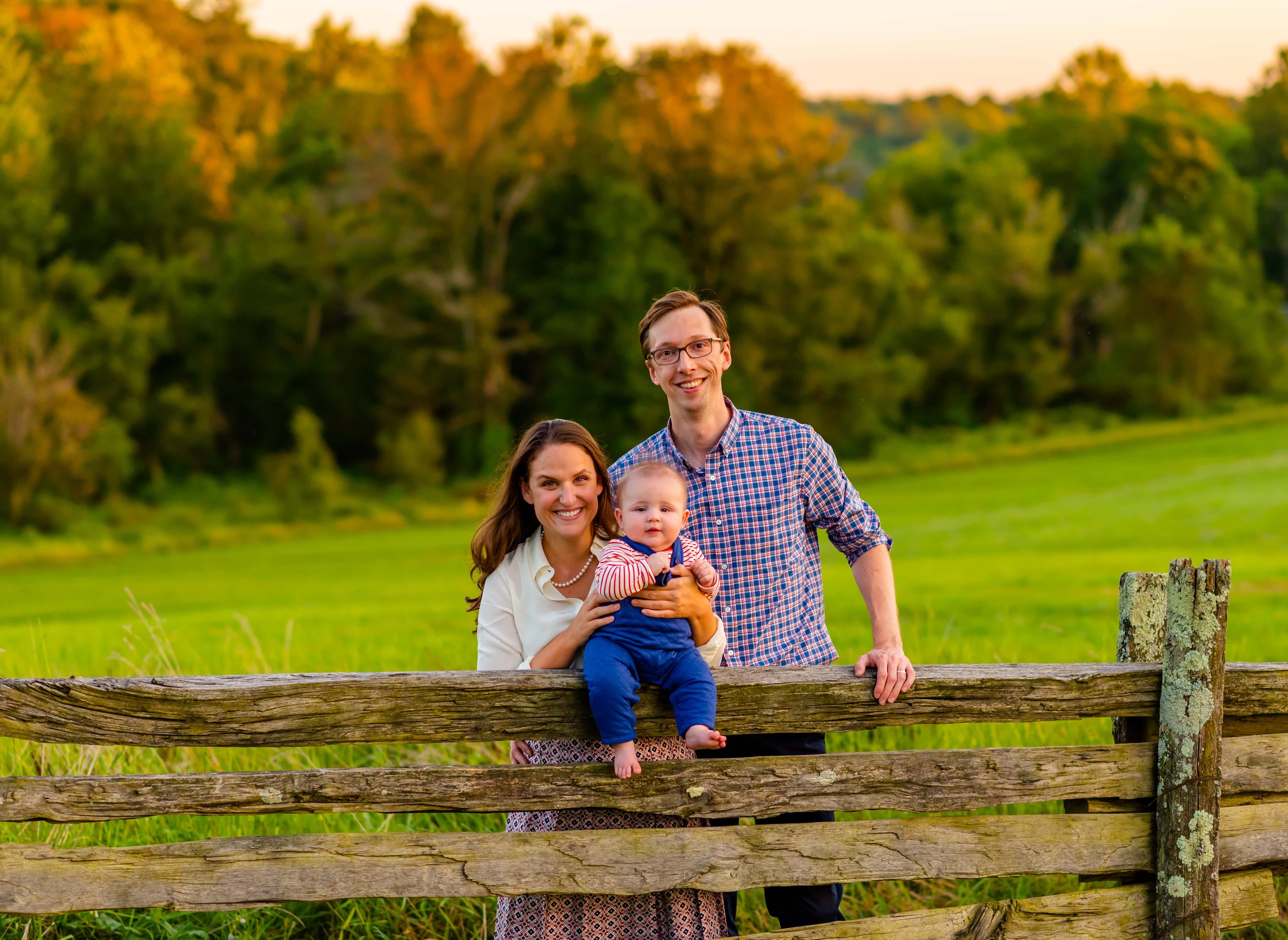 Summer family photo of mom, dad and baby by a fence