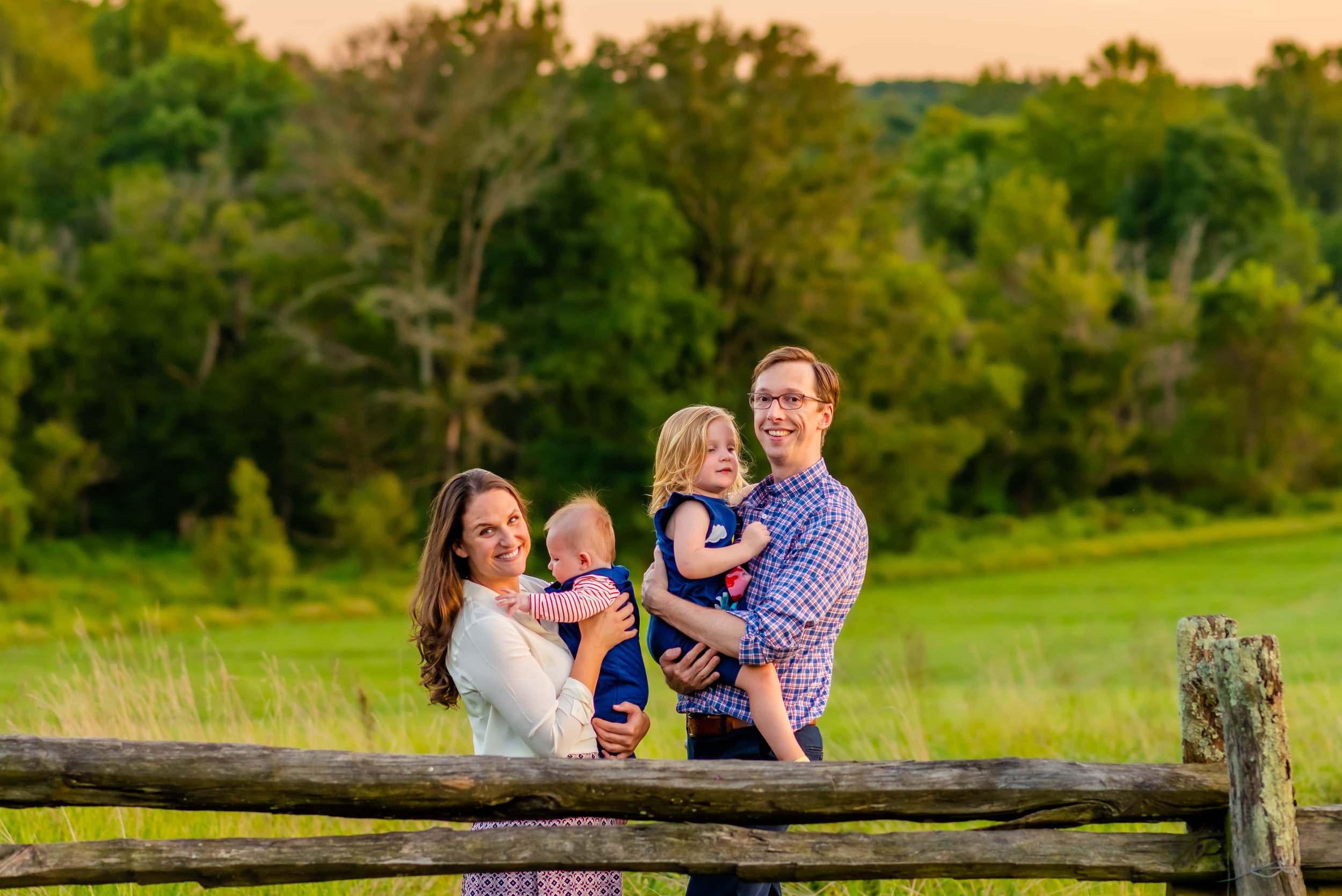 Summer family photo of mom, dad, little girl and baby boy by a fence