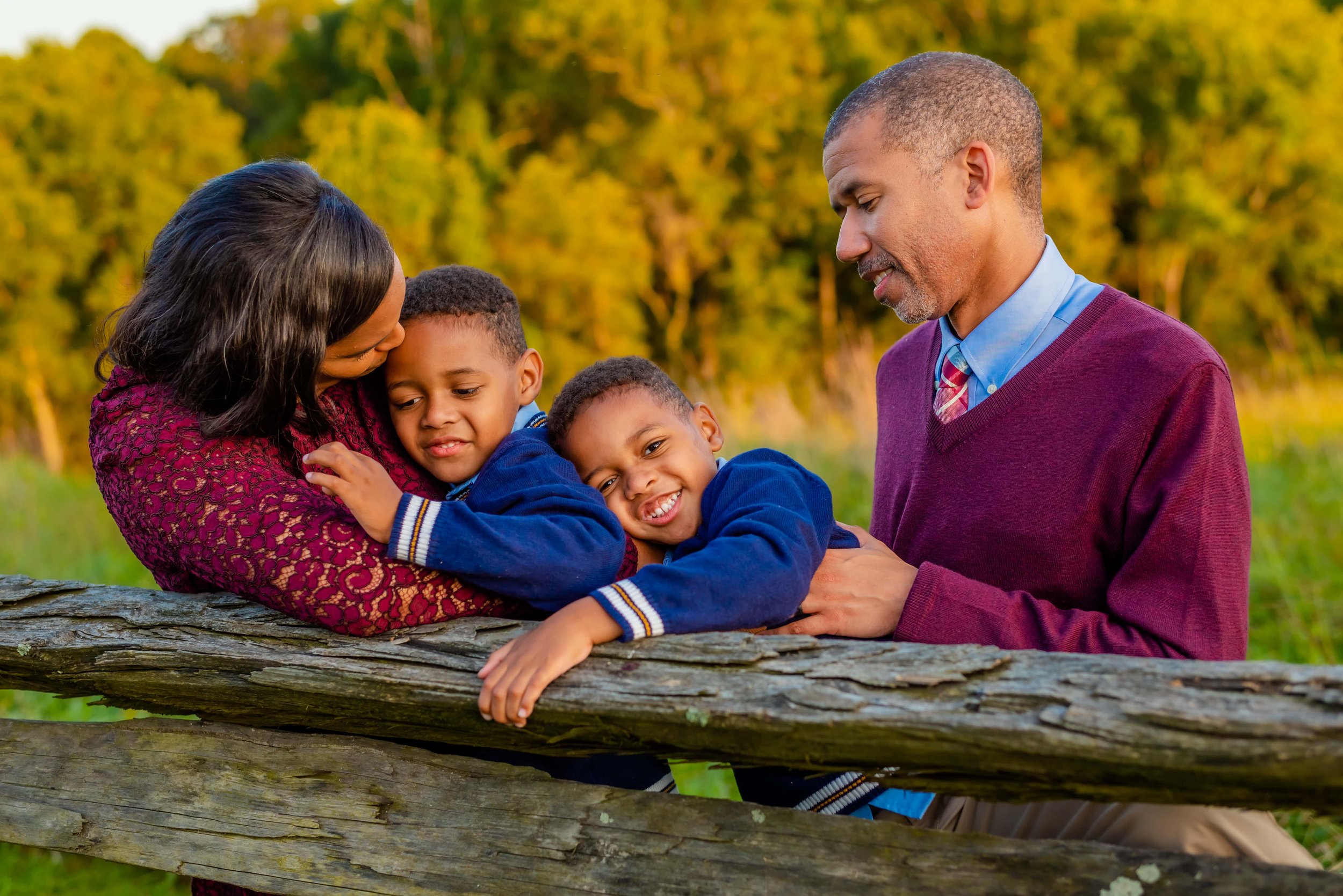 Fall photo of family of mom, dad, and twin sons hugging by a fence
