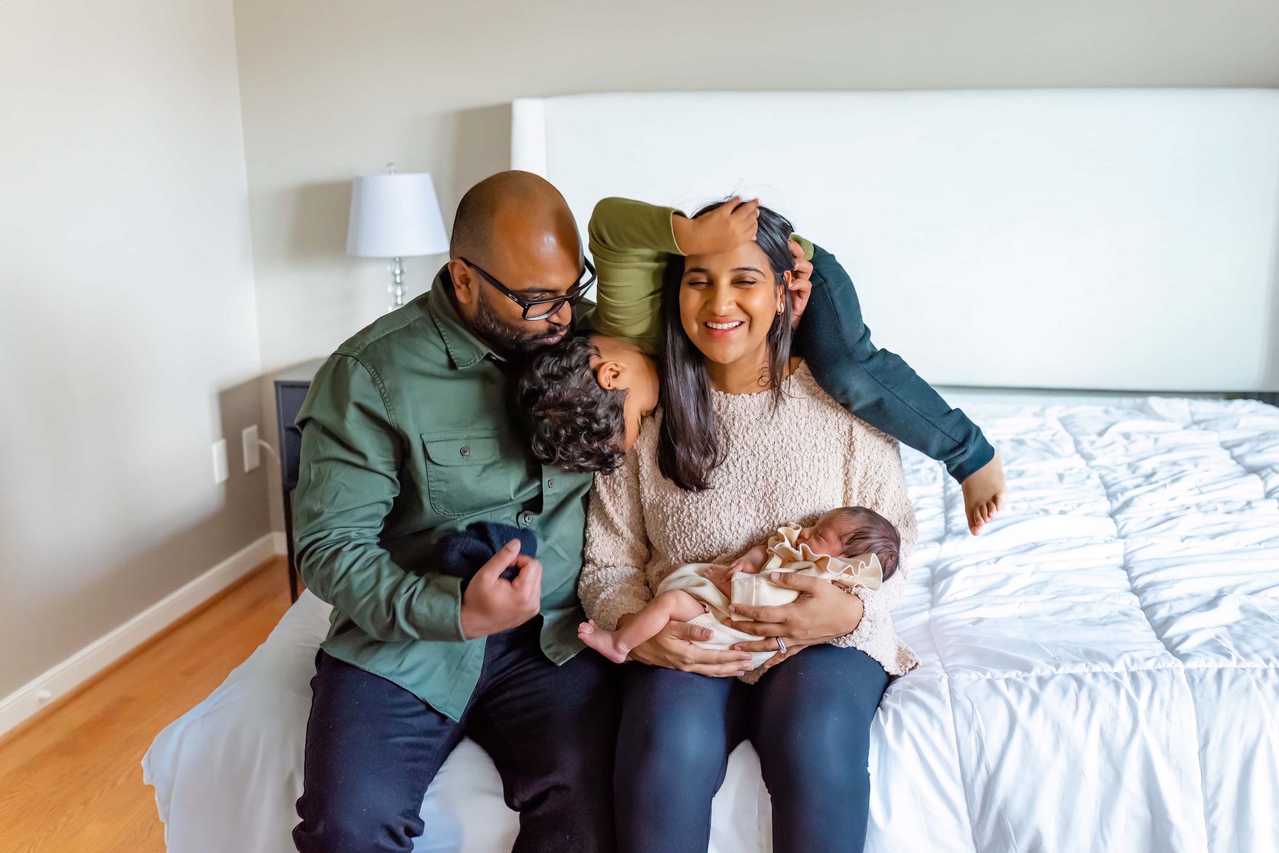 Maryland Newborn Photographer - Mom, dad, toddler and baby playing and laughing on the bed