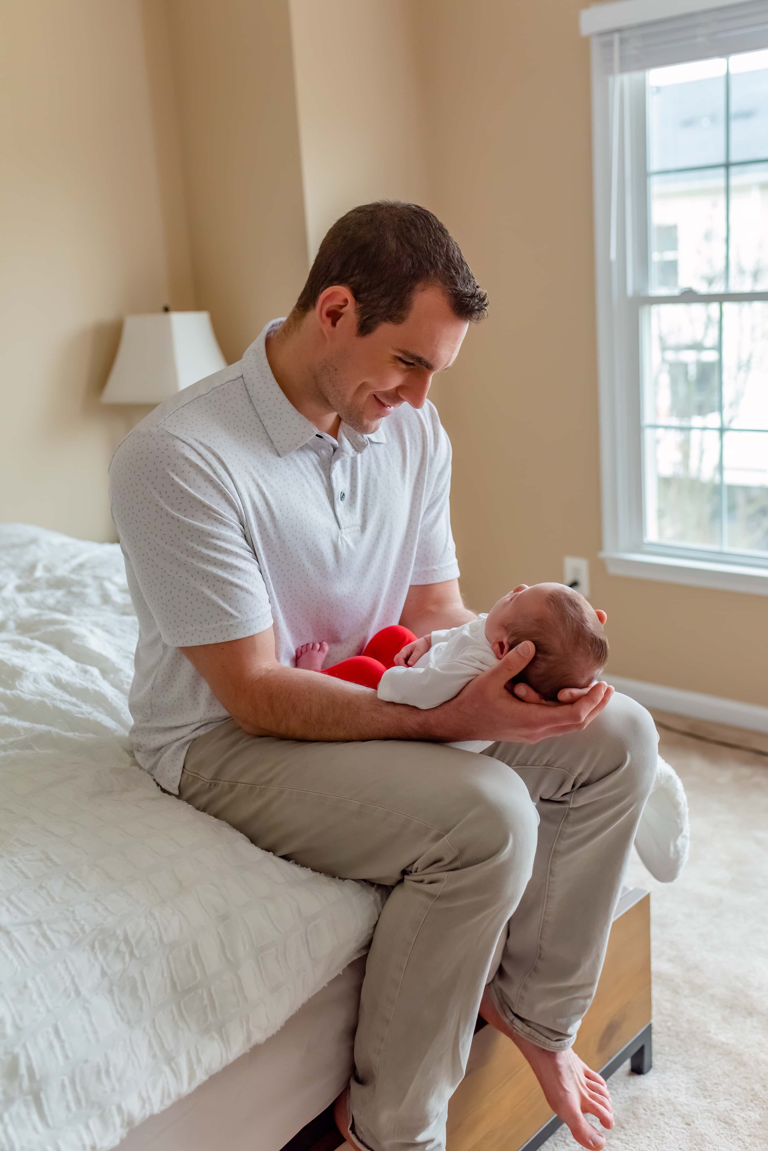 Maryland Lifestyle Newborn Photographer - Dad Sitting on Bed with Baby