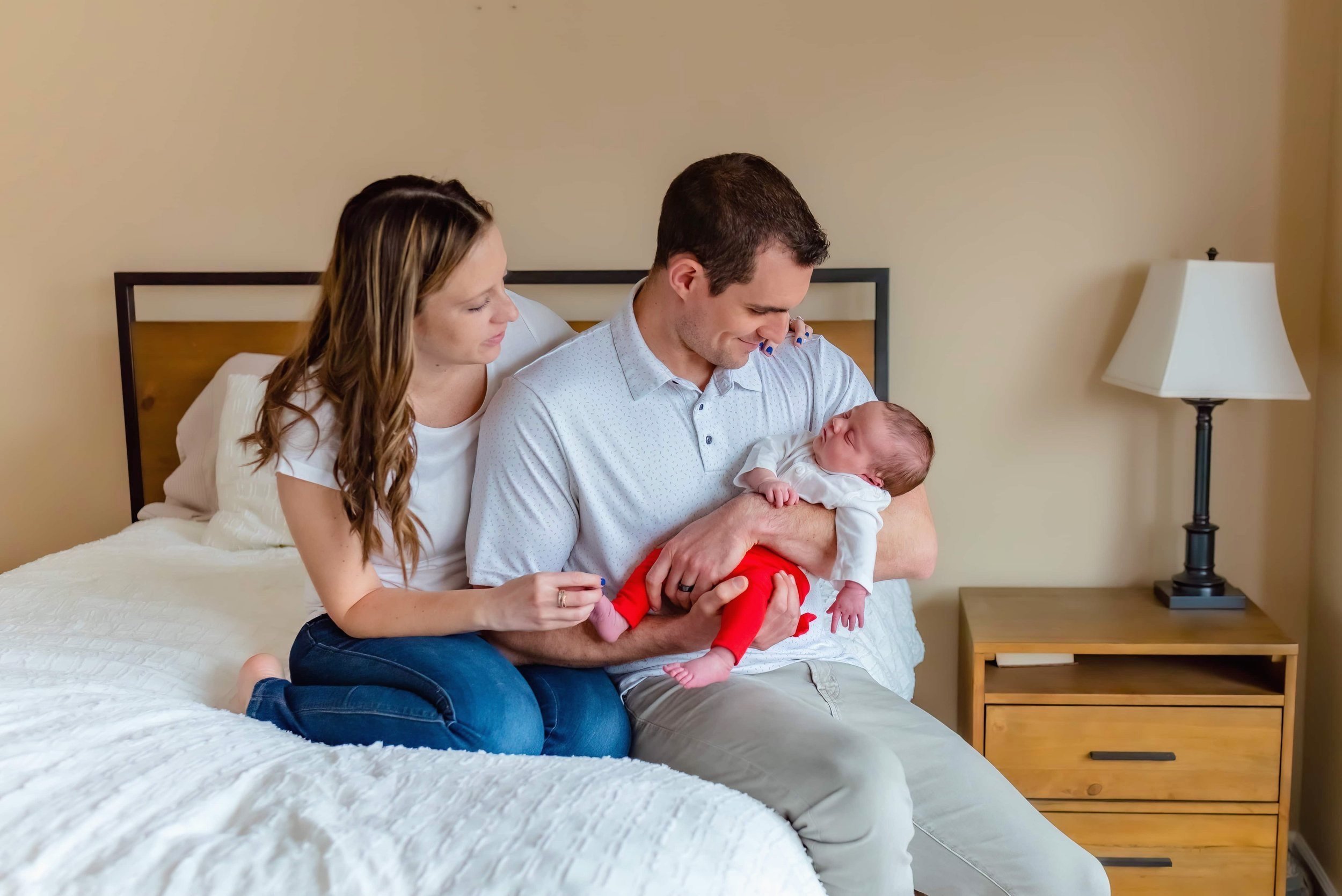 Maryland Lifestyle Newborn Photographer - Mom and dad sitting on a bed with baby 