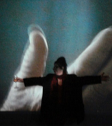 Person standing with arms outstretched in front of a large abstract hand projection on a wall.