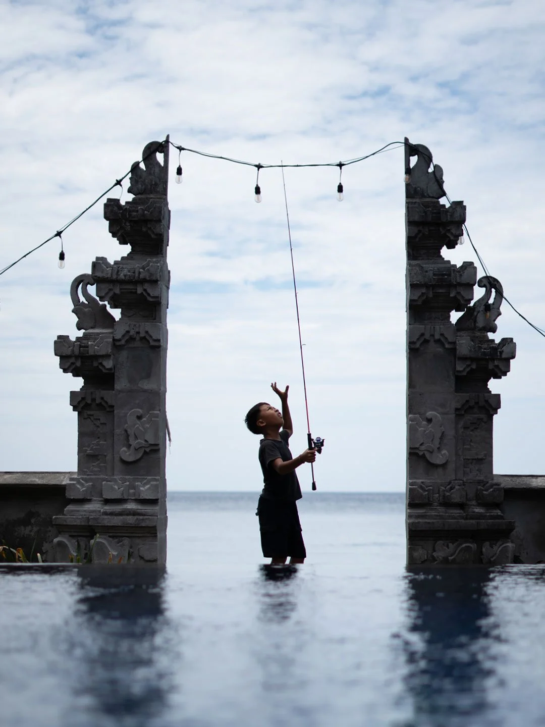 Boy standing between traditional Balinese gates by the sea