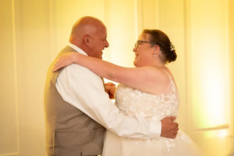 A happy bride and groom share a dance during their wedding reception, smiling and embracing each other.