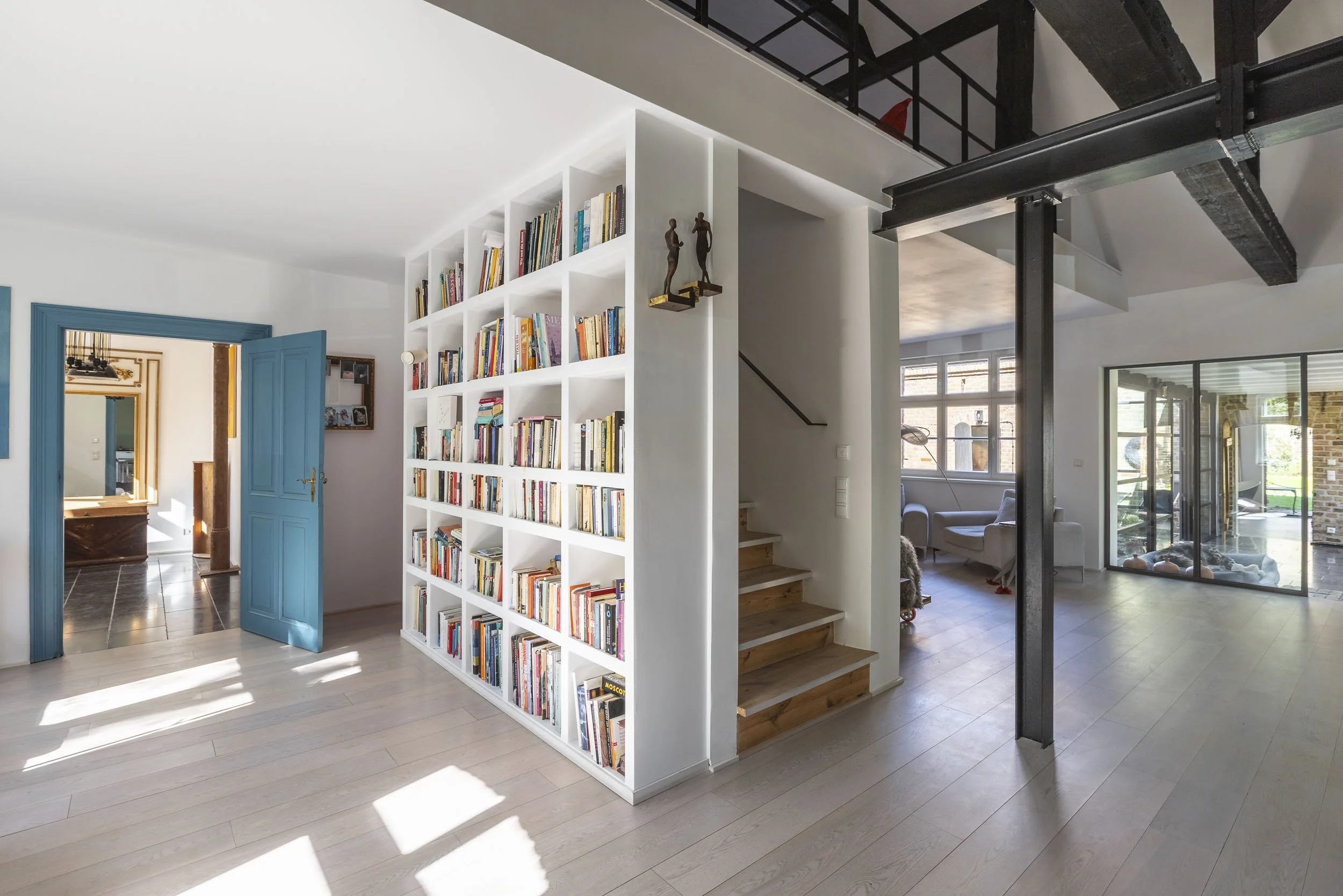 Offener Wohnbereich mit Bibliothek, Treppe und sichtbarer Tragstruktur.